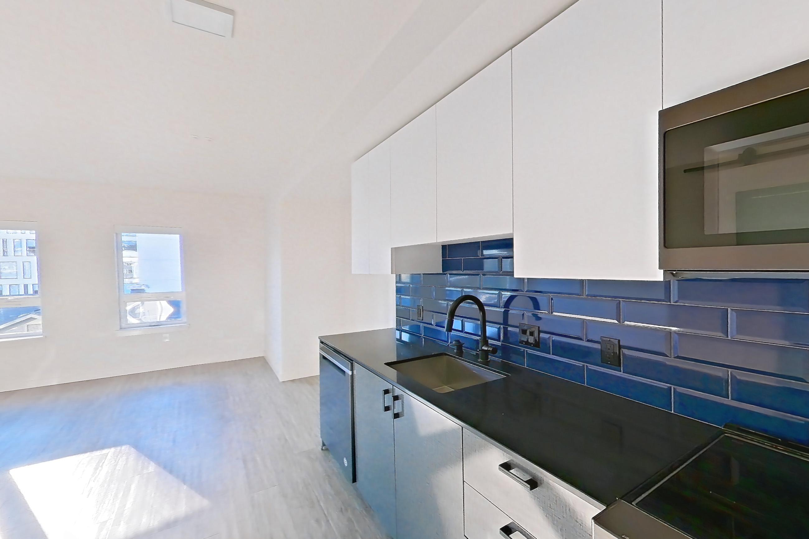 Kitchen with dark countertops, dark stone countertops, dishwasher, light countertops, light wood-finish flooring, microwave, oven/range, refrigerator, and stainless steel appliances, Apartment 604W at Chroma