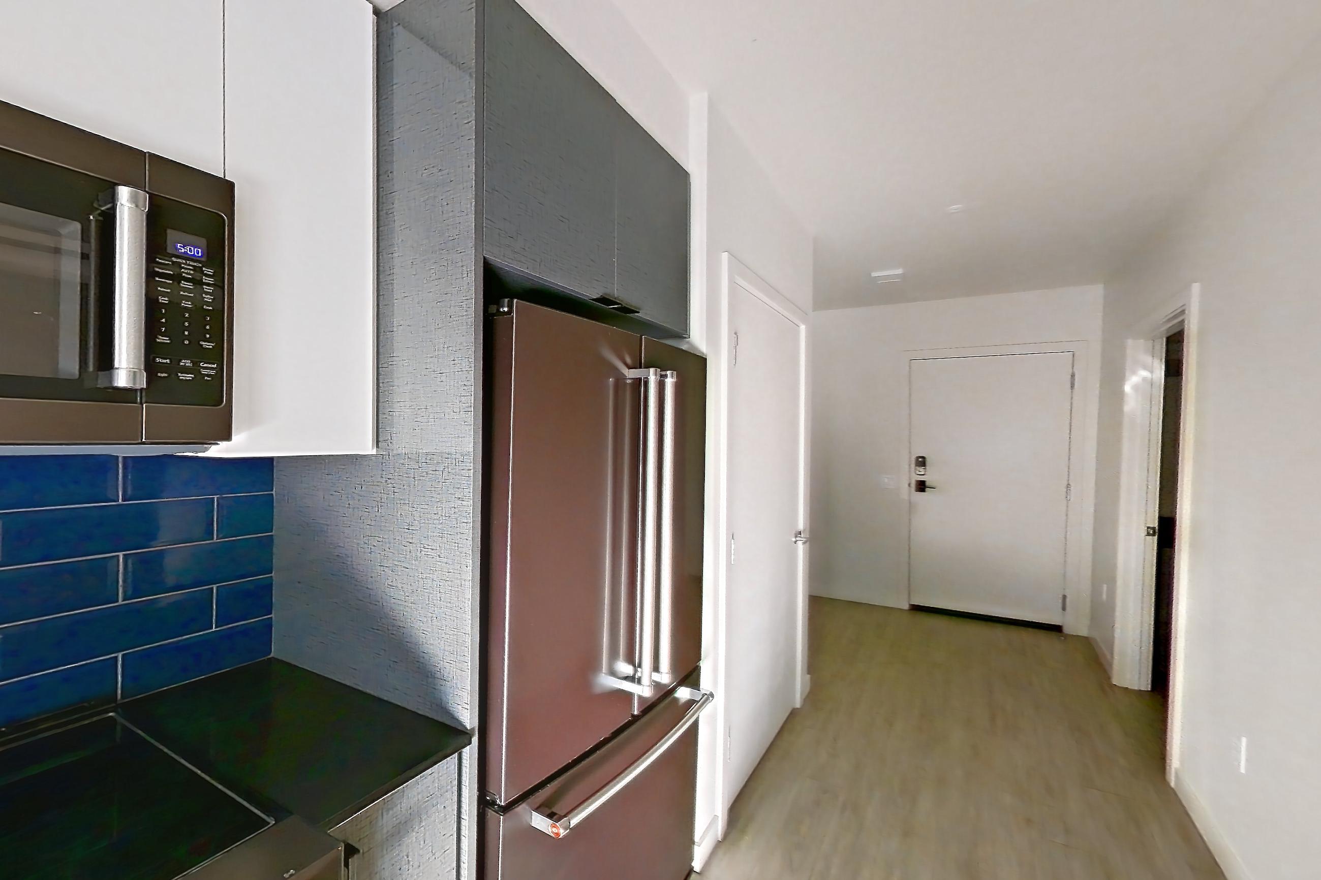Kitchen with dark countertops, dark stone countertops, dishwasher, light countertops, light wood-finish flooring, microwave, oven/range, refrigerator, and stainless steel appliances, Apartment 604W at Chroma