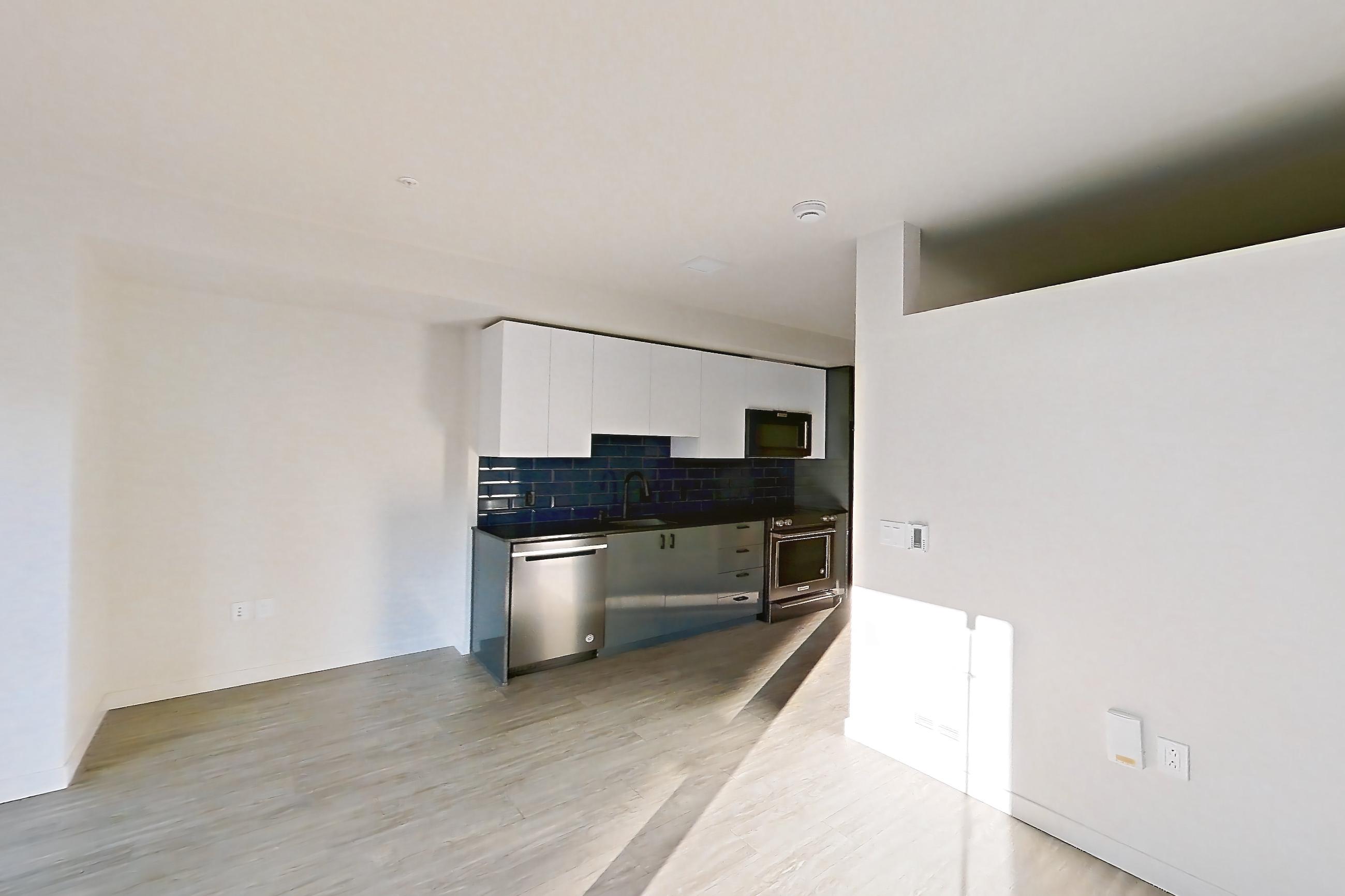 Living room with dark countertops, dark wood-finish flooring, dishwasher, light wood-finish flooring, and stainless steel appliances, Apartment 604W at Chroma