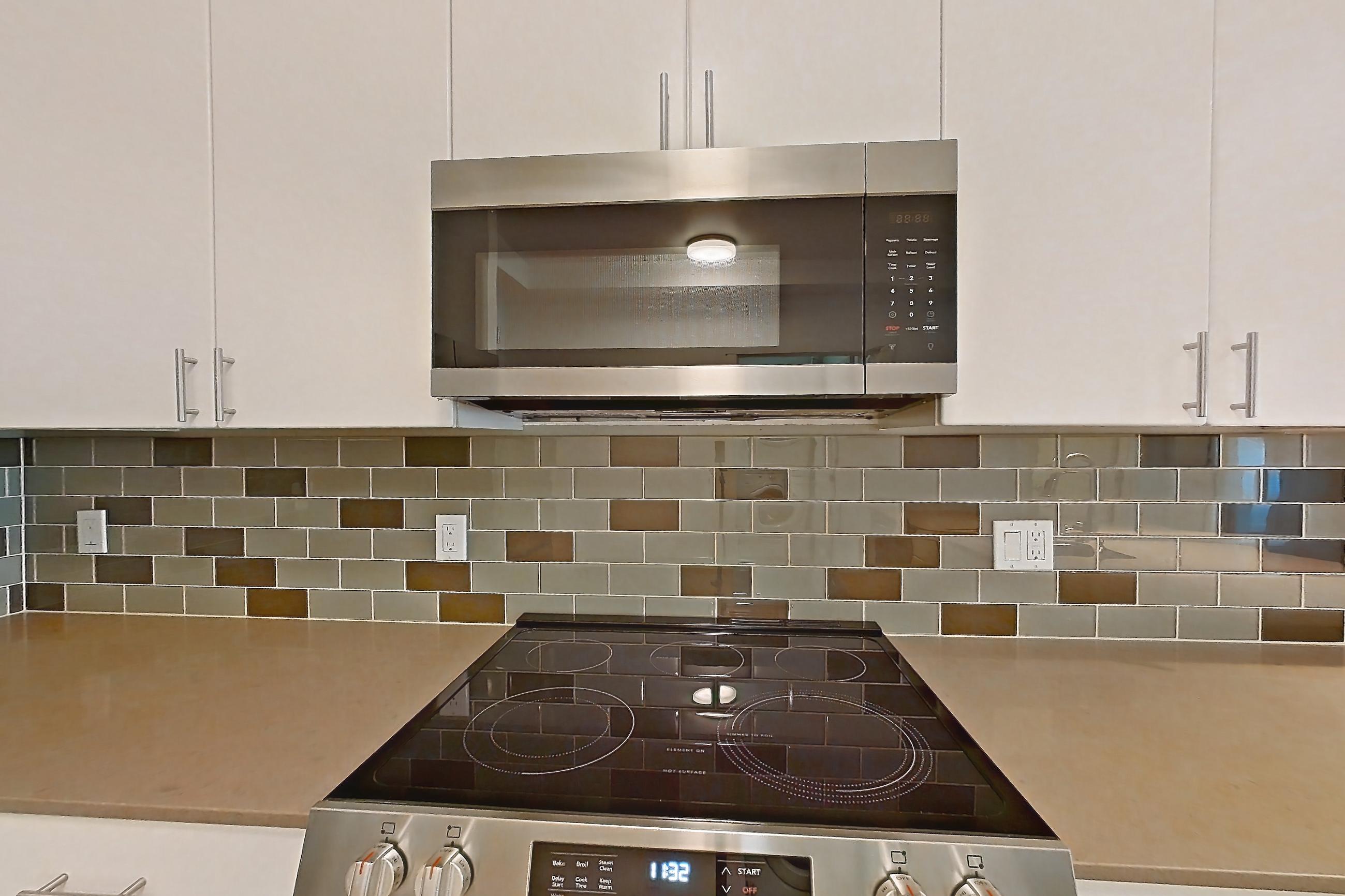 Kitchen with dishwasher, electric range, light countertops, light stone countertops, light wood-finish flooring, microwave, mini-split AC, oven/range, refrigerator, and stainless steel appliances, Unit 228 at The Waymark