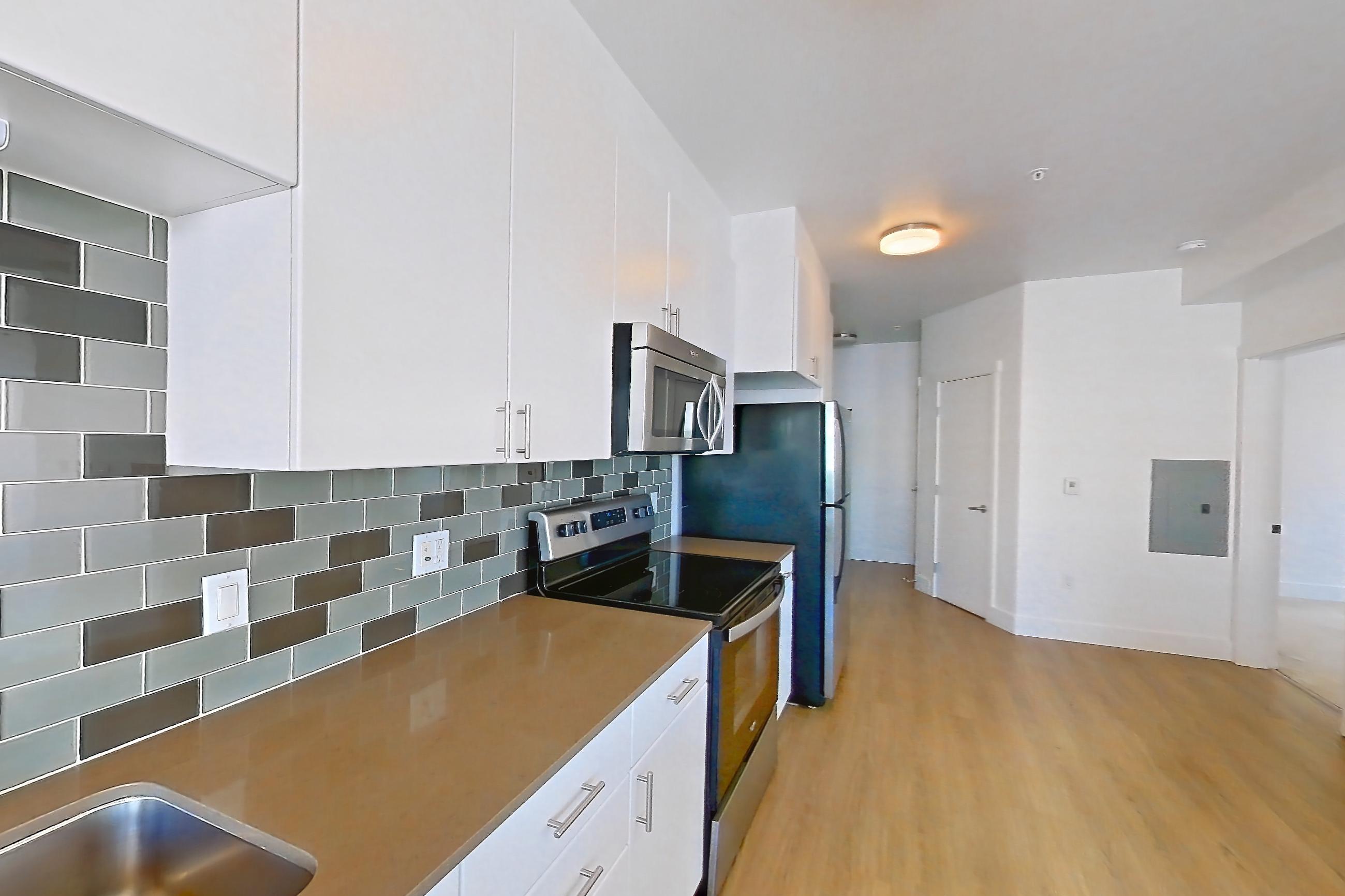Kitchen with dishwasher, electric range, light countertops, light stone countertops, light wood-finish flooring, microwave, oven/range, refrigerator, and stainless steel appliances, Unit 720 at The Waymark