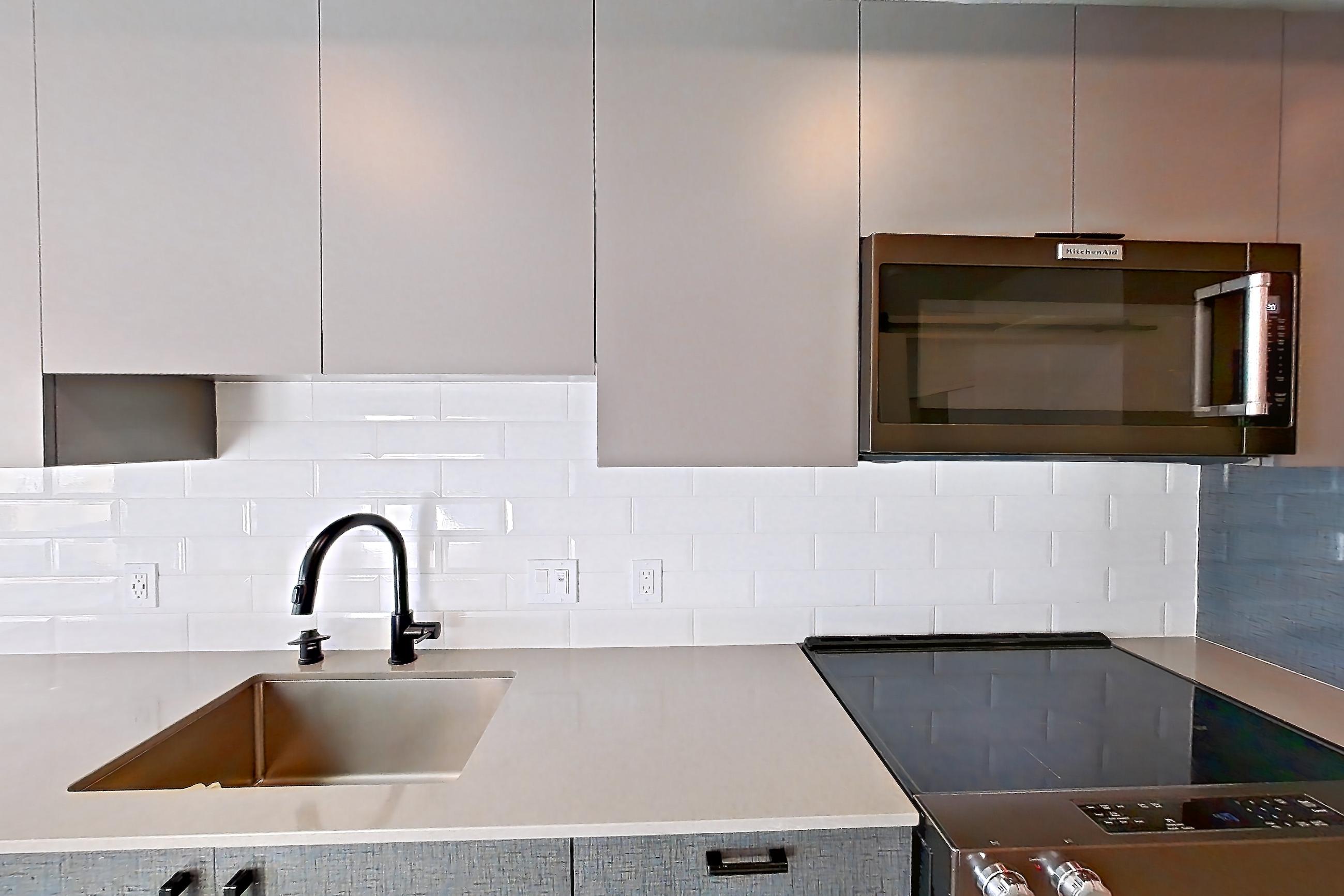 Kitchen with dishwasher, electric range, light countertops, light stone countertops, light wood-finish flooring, oven/range, refrigerator, stainless steel appliances, and water & ice dispenser, Apartment 515 at Chroma