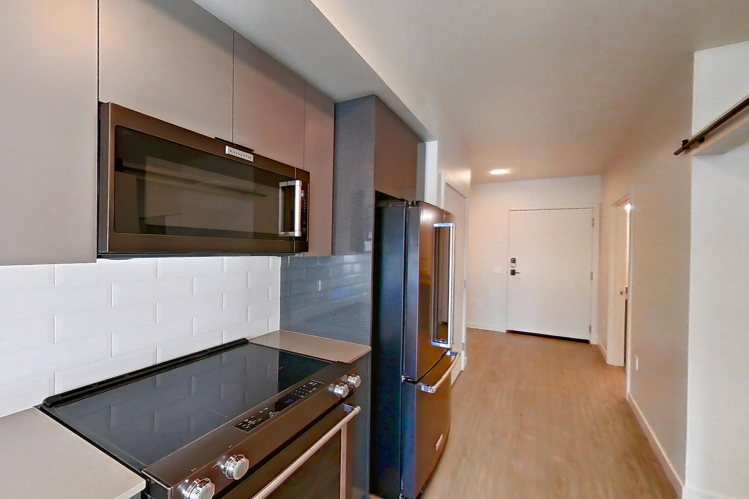 Kitchen with dishwasher, electric range, light countertops, light stone countertops, light wood-finish flooring, oven/range, refrigerator, stainless steel appliances, and water & ice dispenser, Apartment 515 at Chroma
