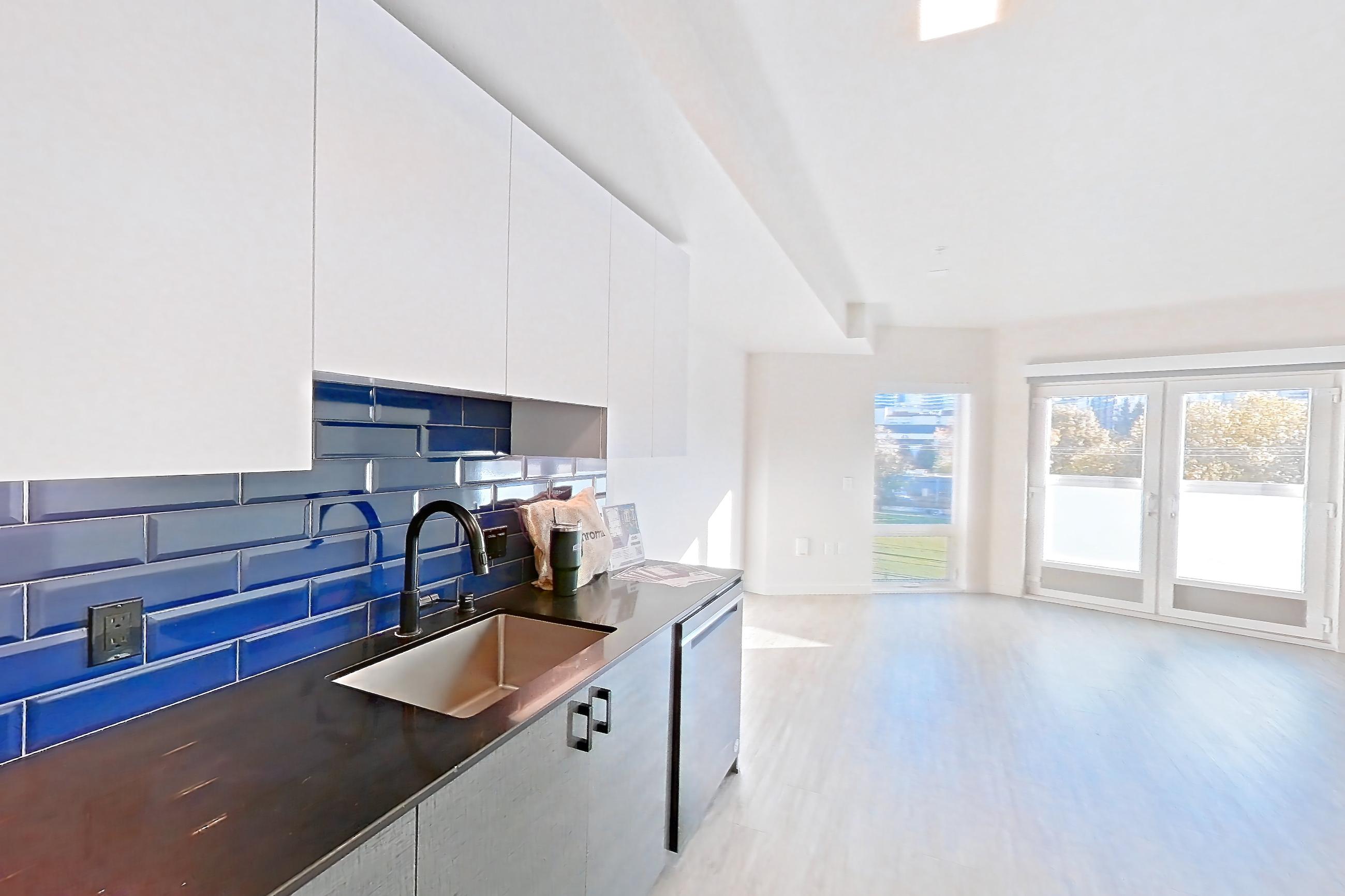 Kitchen with dark countertops, dishwasher, electric range, light countertops, light wood-finish flooring, microwave, oven/range, refrigerator, stainless steel appliances, and water & ice dispenser, Apartment 416 at Chroma