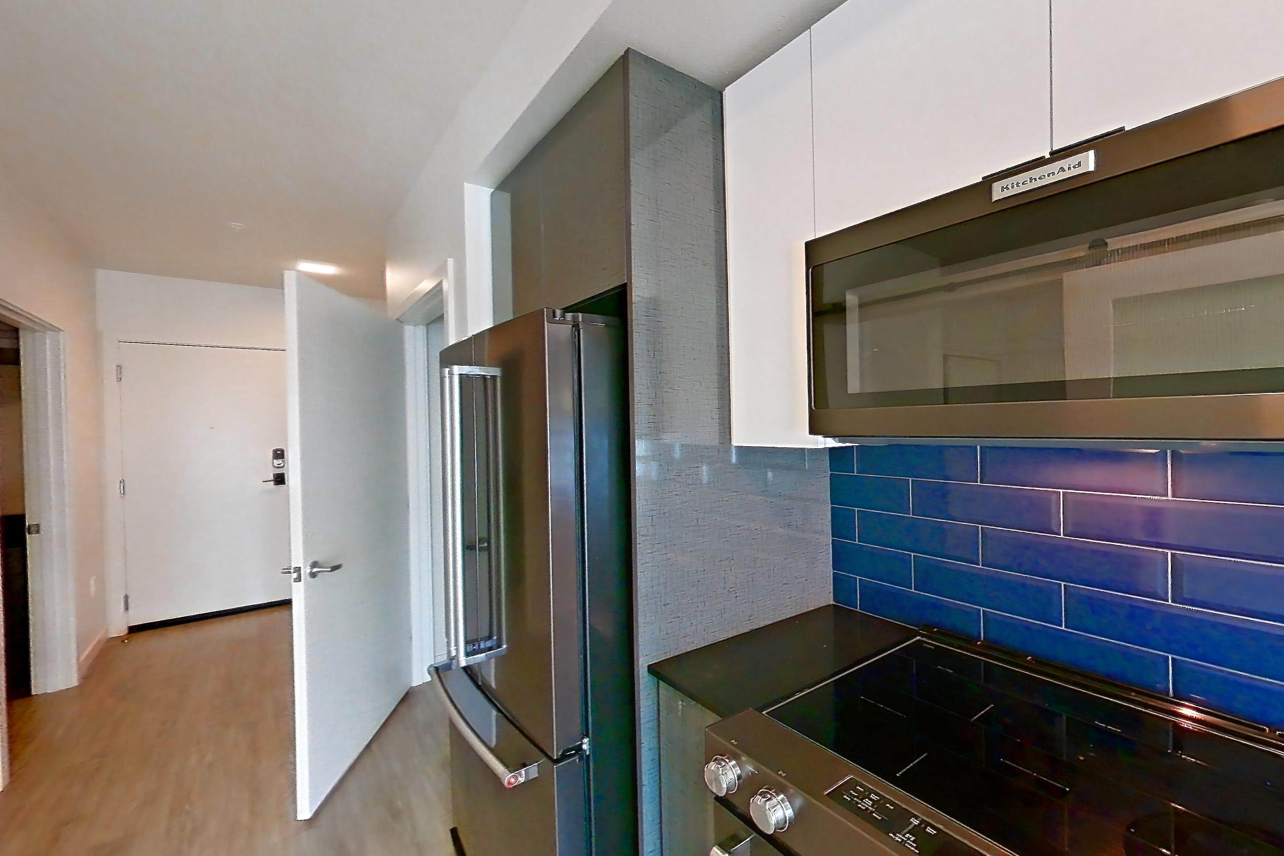 Kitchen with dark countertops, dishwasher, electric range, light countertops, light wood-finish flooring, microwave, oven/range, refrigerator, stainless steel appliances, and water & ice dispenser, Apartment 416 at Chroma