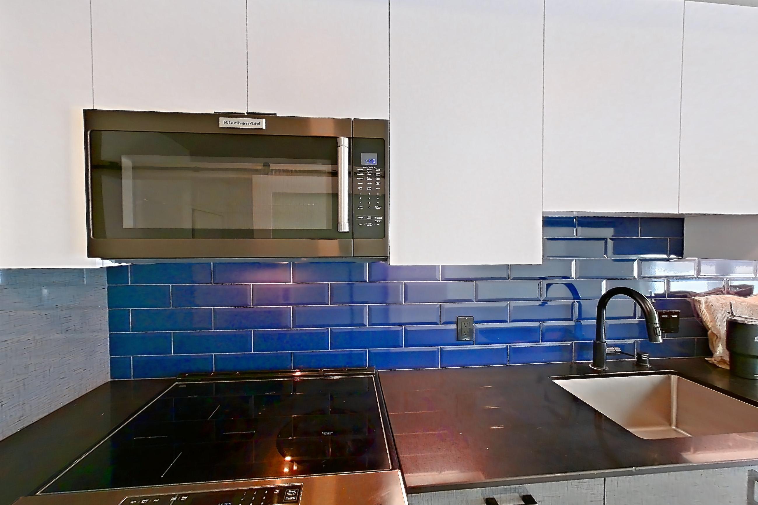 Kitchen with dark countertops, dishwasher, electric range, light countertops, light wood-finish flooring, microwave, oven/range, refrigerator, stainless steel appliances, and water & ice dispenser, Apartment 416 at Chroma
