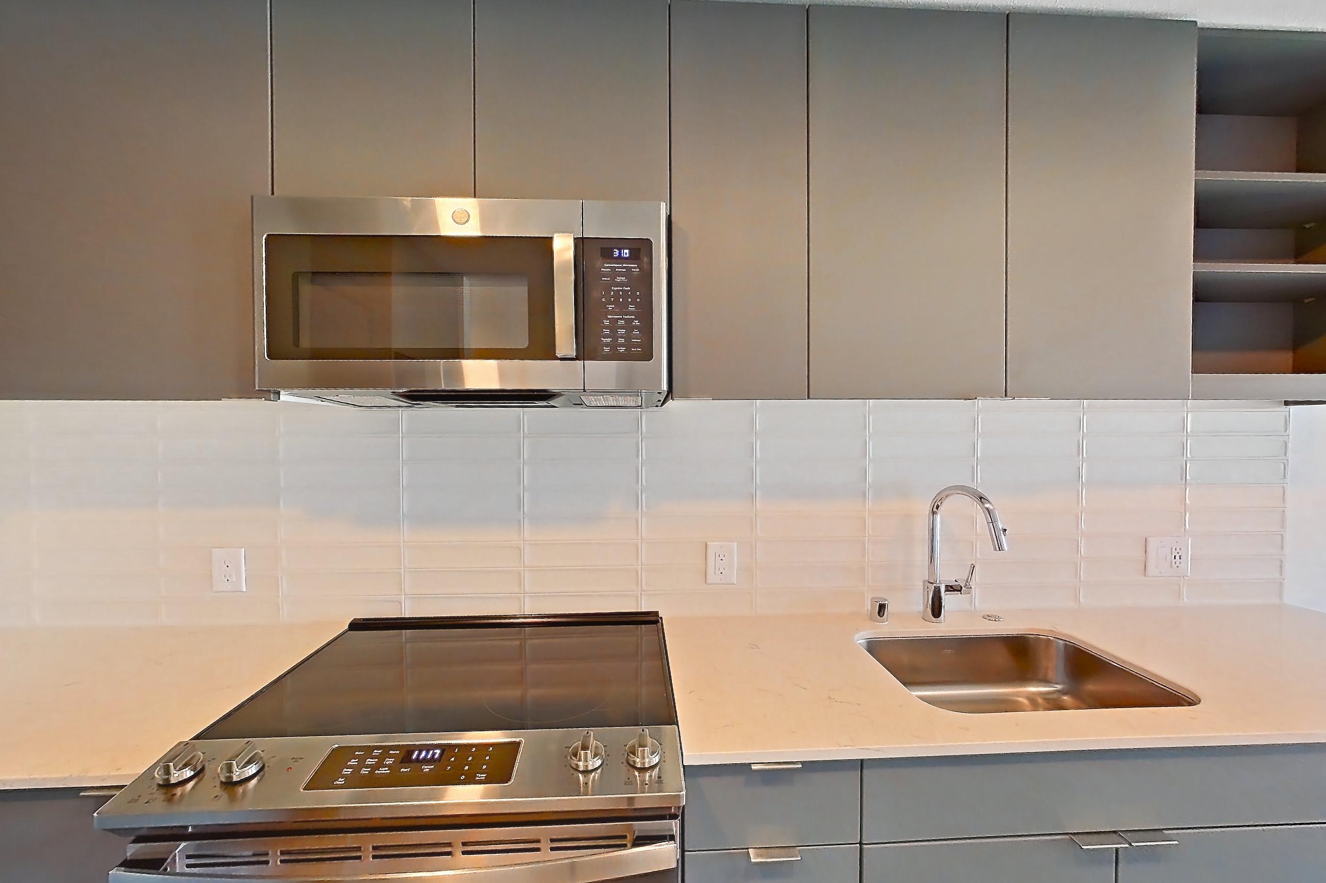 Kitchen with electric range, light countertops, light stone countertops, light wood-finish flooring, microwave, oven/range, refrigerator, and stainless steel appliances, Unit 180 at Arlo