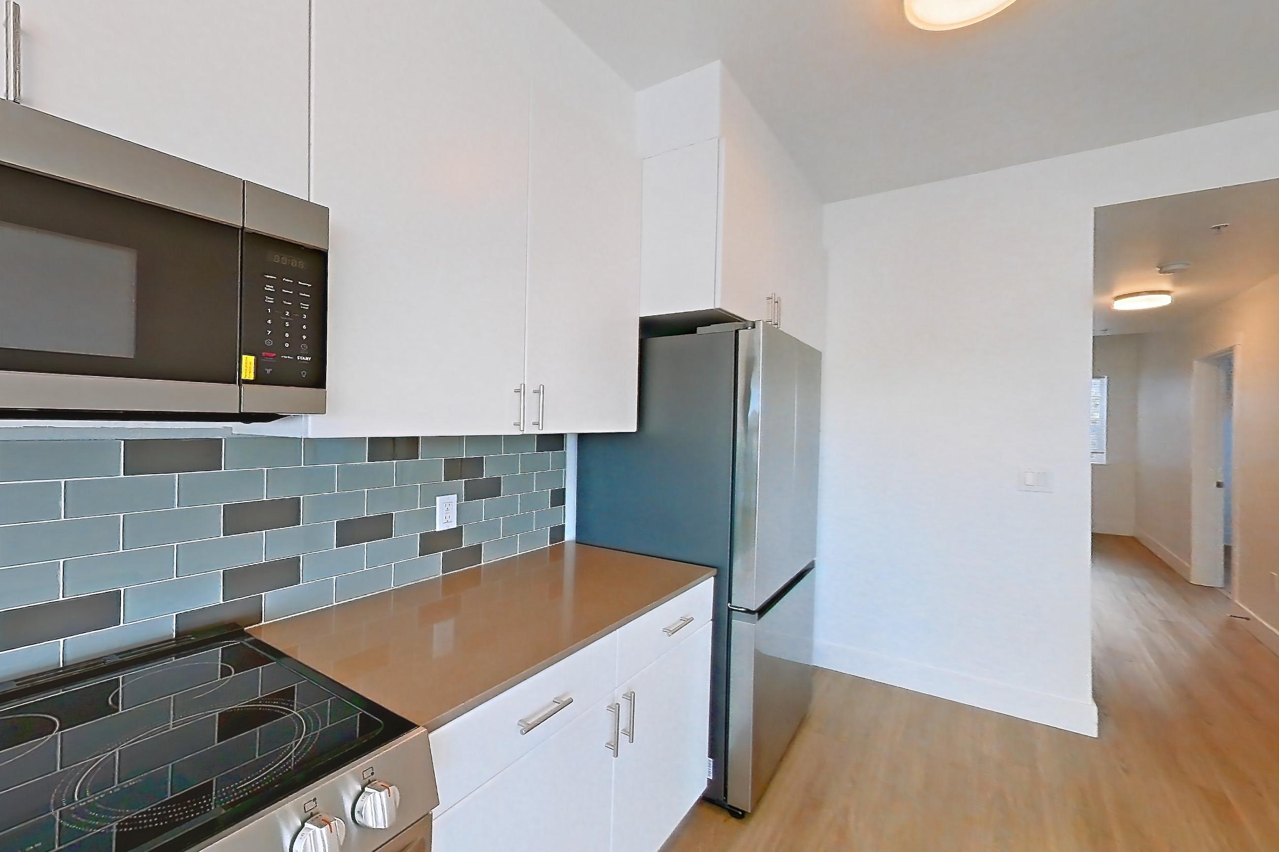 Kitchen with dishwasher, electric range, light countertops, light stone countertops, light wood-finish flooring, microwave, oven/range, refrigerator, and stainless steel appliances, Unit 307 at The Waymark