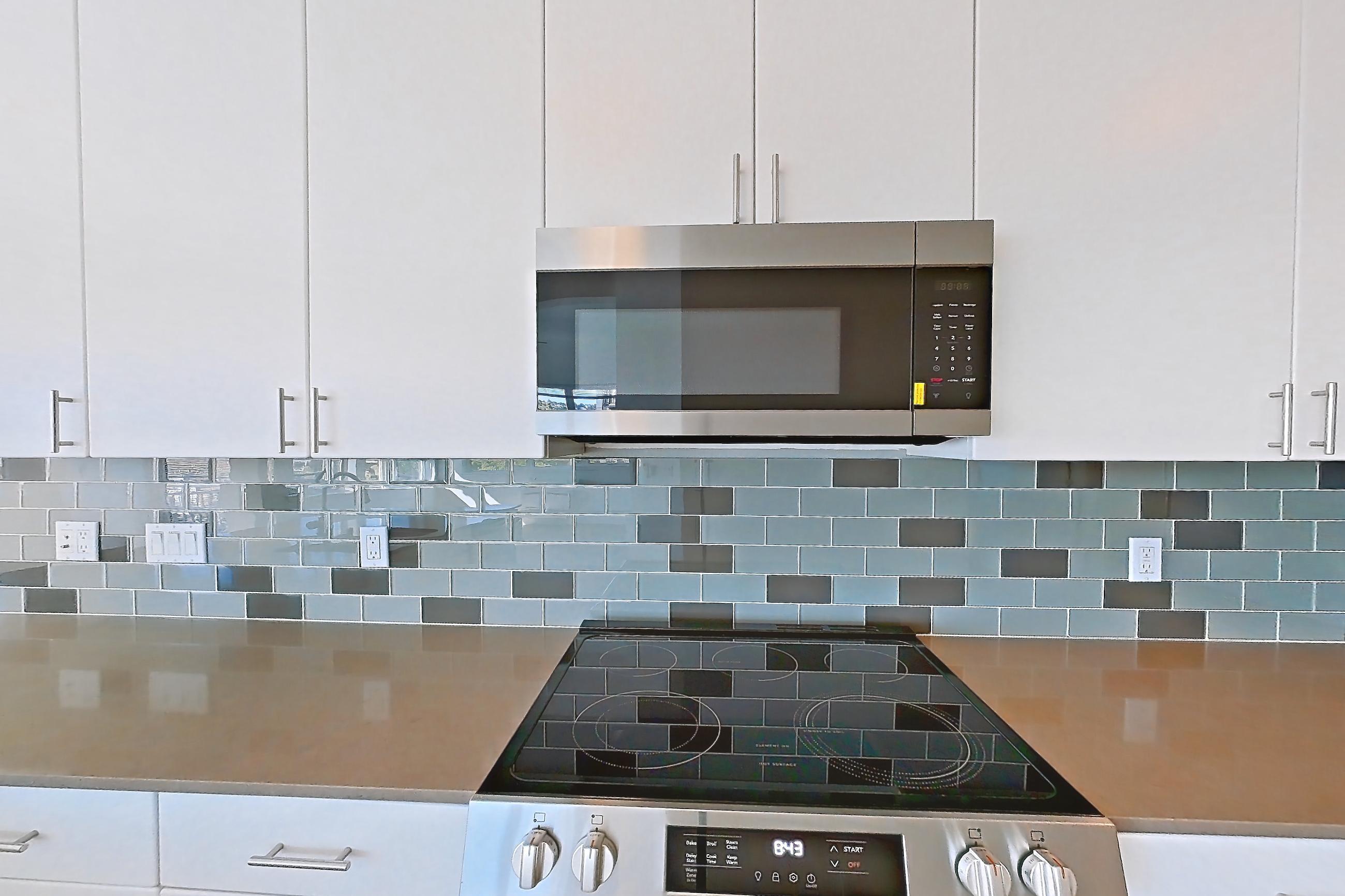 Kitchen with dishwasher, electric range, light countertops, light stone countertops, light wood-finish flooring, microwave, oven/range, refrigerator, and stainless steel appliances, Unit 307 at The Waymark