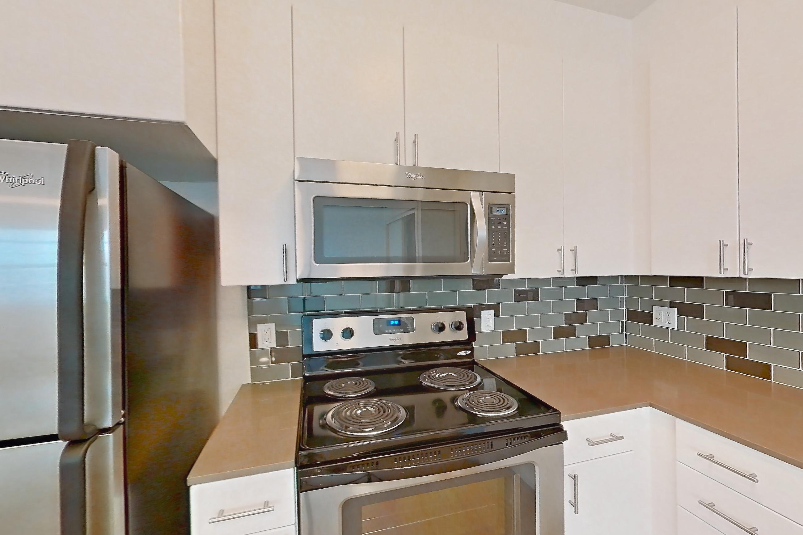 Kitchen with baseboard heating, dishwasher, electric range, light countertops, light wood-finish flooring, microwave, oven/range, refrigerator, and stainless steel appliances, Unit 501 at The Waymark