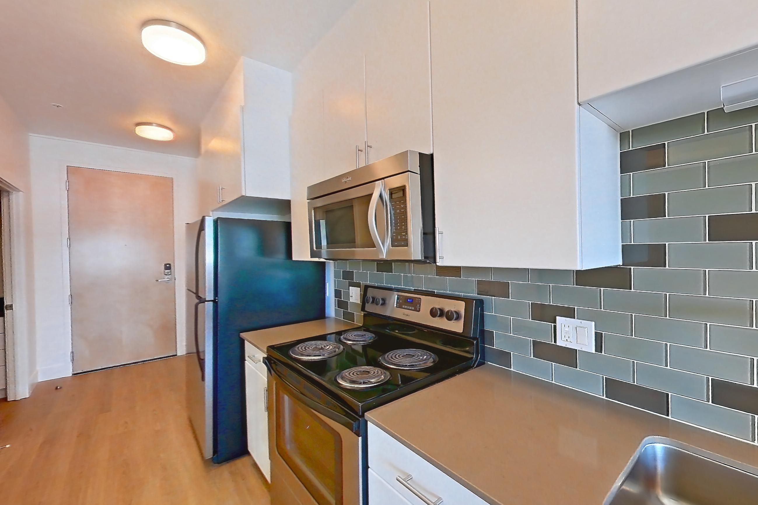 Kitchen with baseboard heating, black appliances, dishwasher, electric range, light countertops, light wood-finish flooring, oven/range, refrigerator, and stainless steel appliances, Unit 825 at The Waymark
