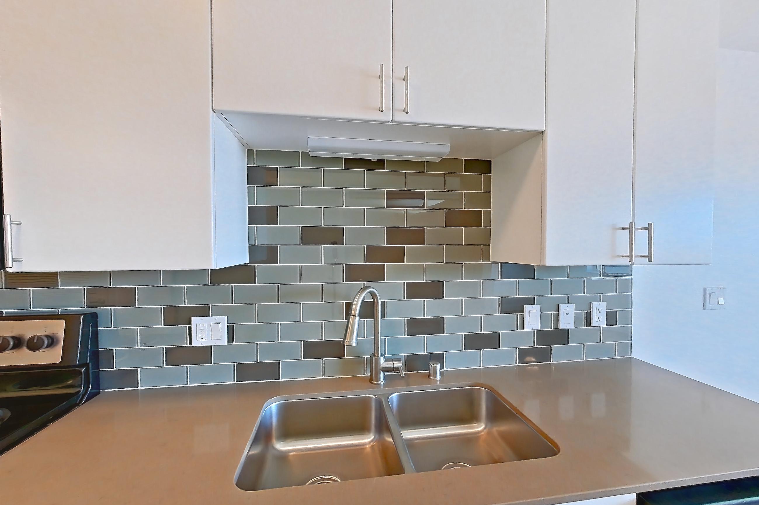 Kitchen with baseboard heating, black appliances, dishwasher, electric range, light countertops, light wood-finish flooring, oven/range, refrigerator, and stainless steel appliances, Unit 825 at The Waymark