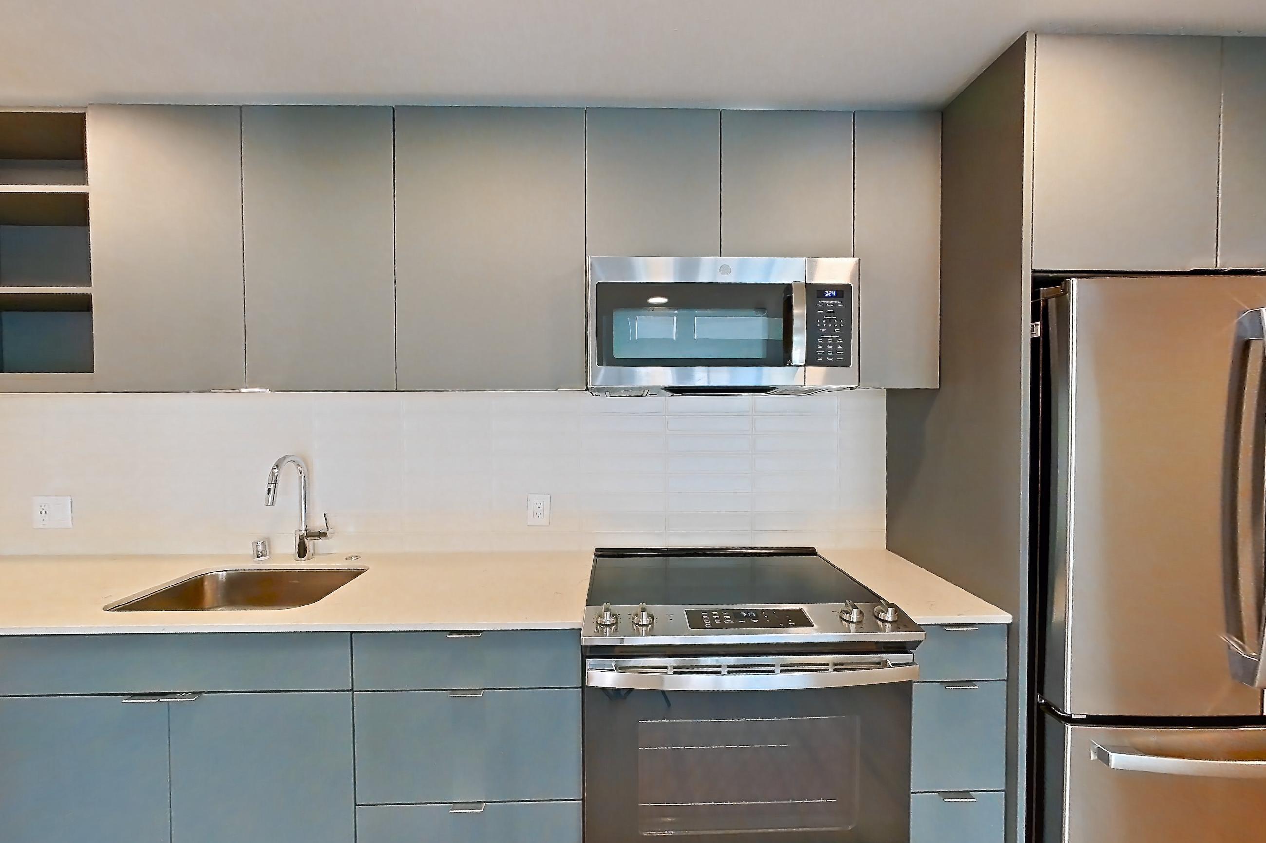 Kitchen with dishwasher, electric range, light countertops, light stone countertops, light wood-finish flooring, microwave, oven/range, refrigerator, and stainless steel appliances, Unit 130 at Arlo