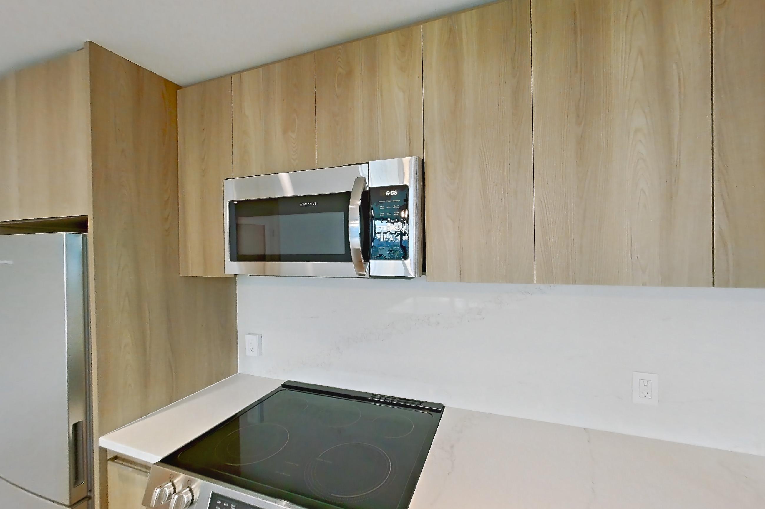 Kitchen with electric range, light countertops, light stone countertops, light wood-finish flooring, microwave, oven/range, refrigerator, and stainless steel appliances, Unit 0605 at Hearthstone