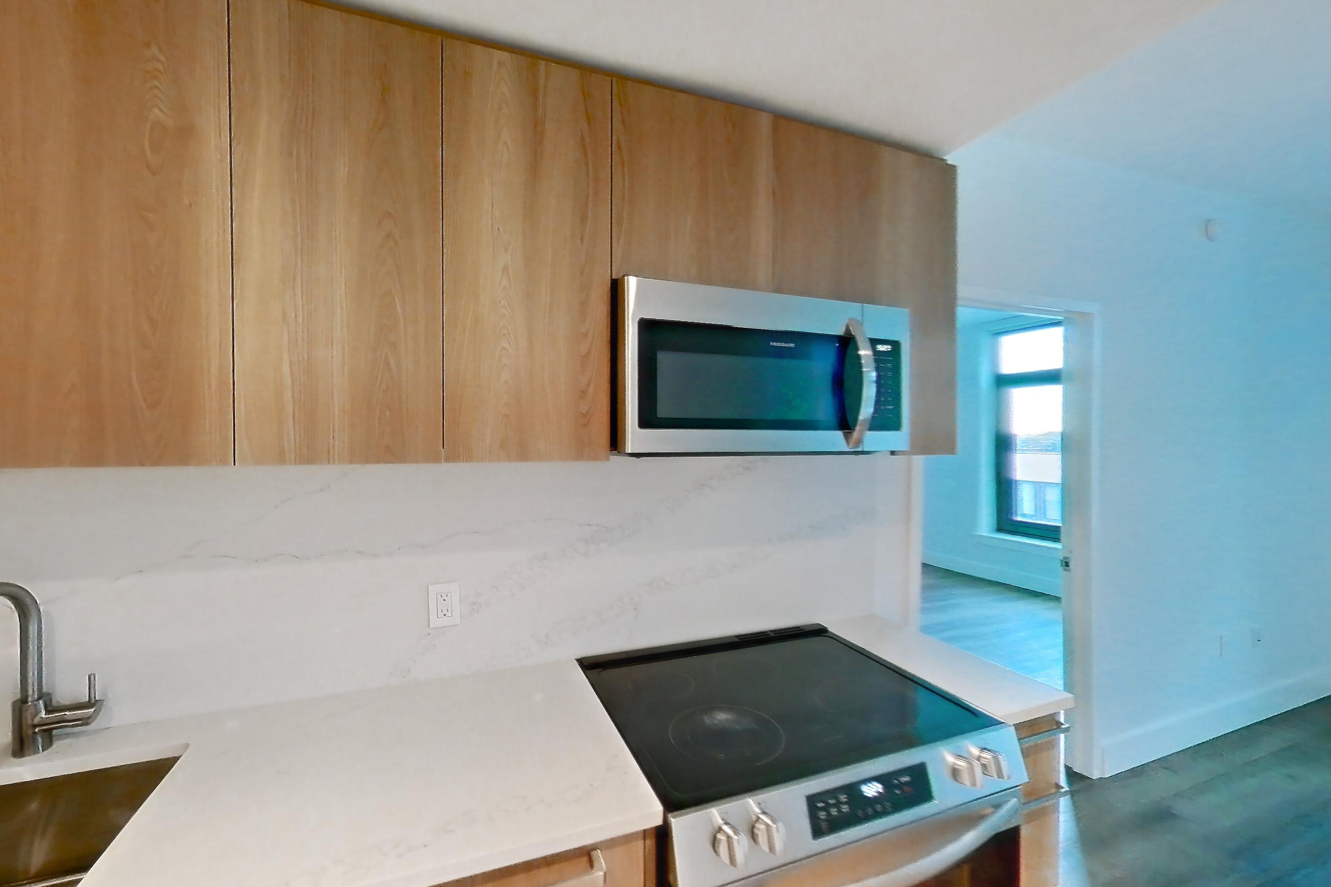 Kitchen with cooktop, electric cooktop, electric range, light stone countertops, light wood-finish flooring, microwave, oven/range, refrigerator, and stainless steel appliances, Unit 0626 at Hearthstone