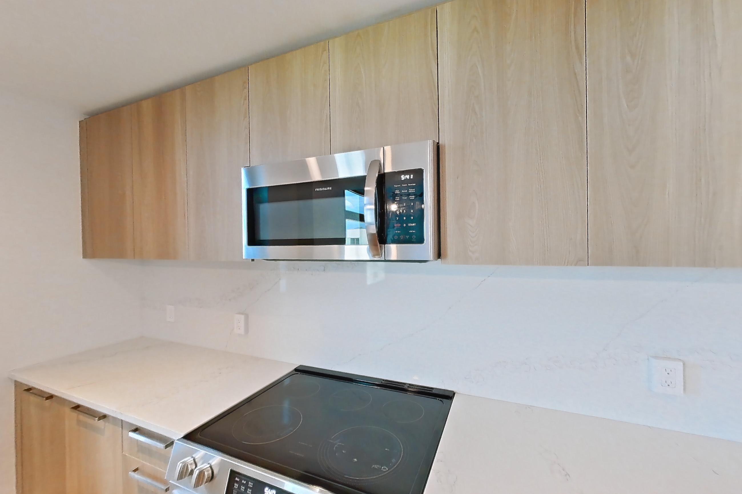 Kitchen with electric range, light countertops, light stone countertops, light wood-finish flooring, microwave, oven/range, refrigerator, and stainless steel appliances, Unit 0625 at Hearthstone