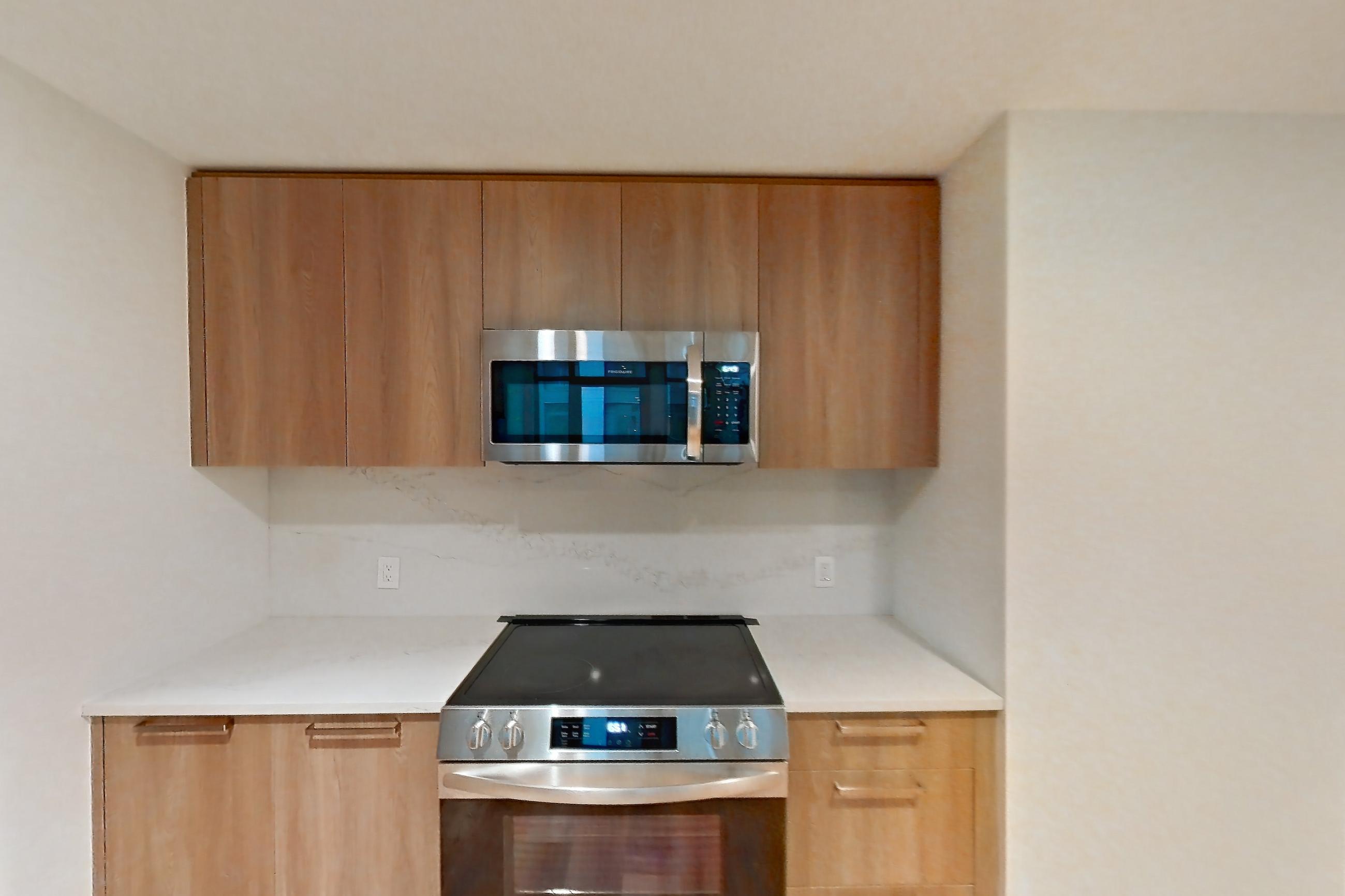 Kitchen with electric range, light countertops, light stone countertops, light wood-finish flooring, microwave, oven/range, refrigerator, and stainless steel appliances, Unit 0231 at Hearthstone