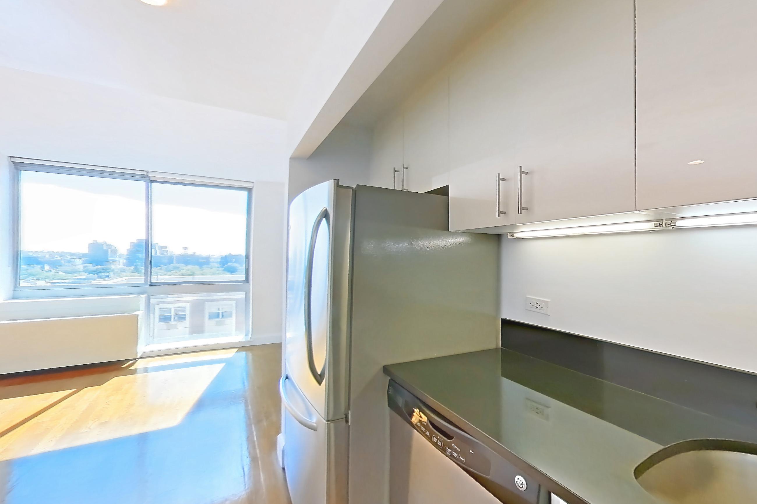 Kitchen with dark countertops, dishwasher, gas range, light countertops, light wood-finish flooring, microwave, oven/range, refrigerator, stainless steel appliances, and white appliances, Apartment 10M at The Addison