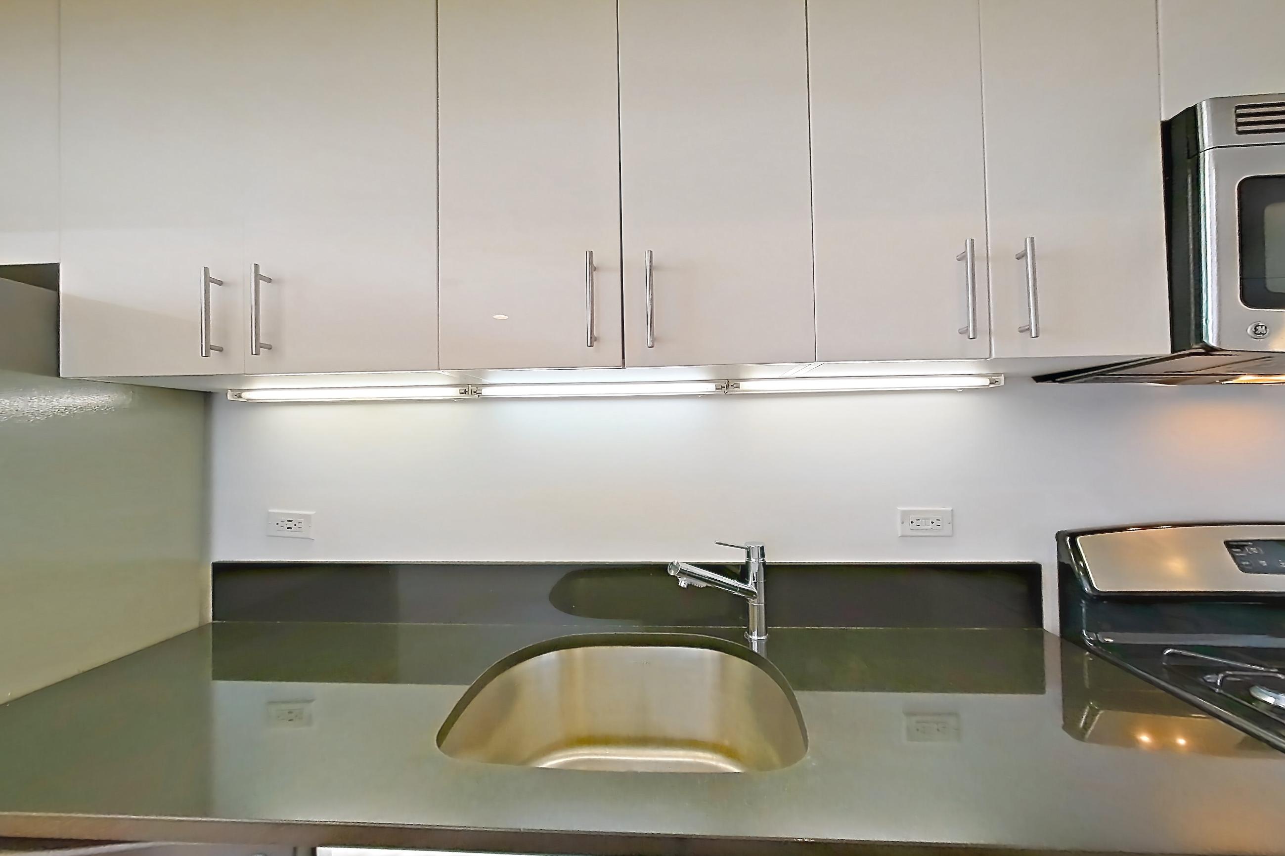 Kitchen with dark countertops, dishwasher, gas range, light countertops, light wood-finish flooring, microwave, oven/range, refrigerator, stainless steel appliances, and white appliances, Apartment 10M at The Addison