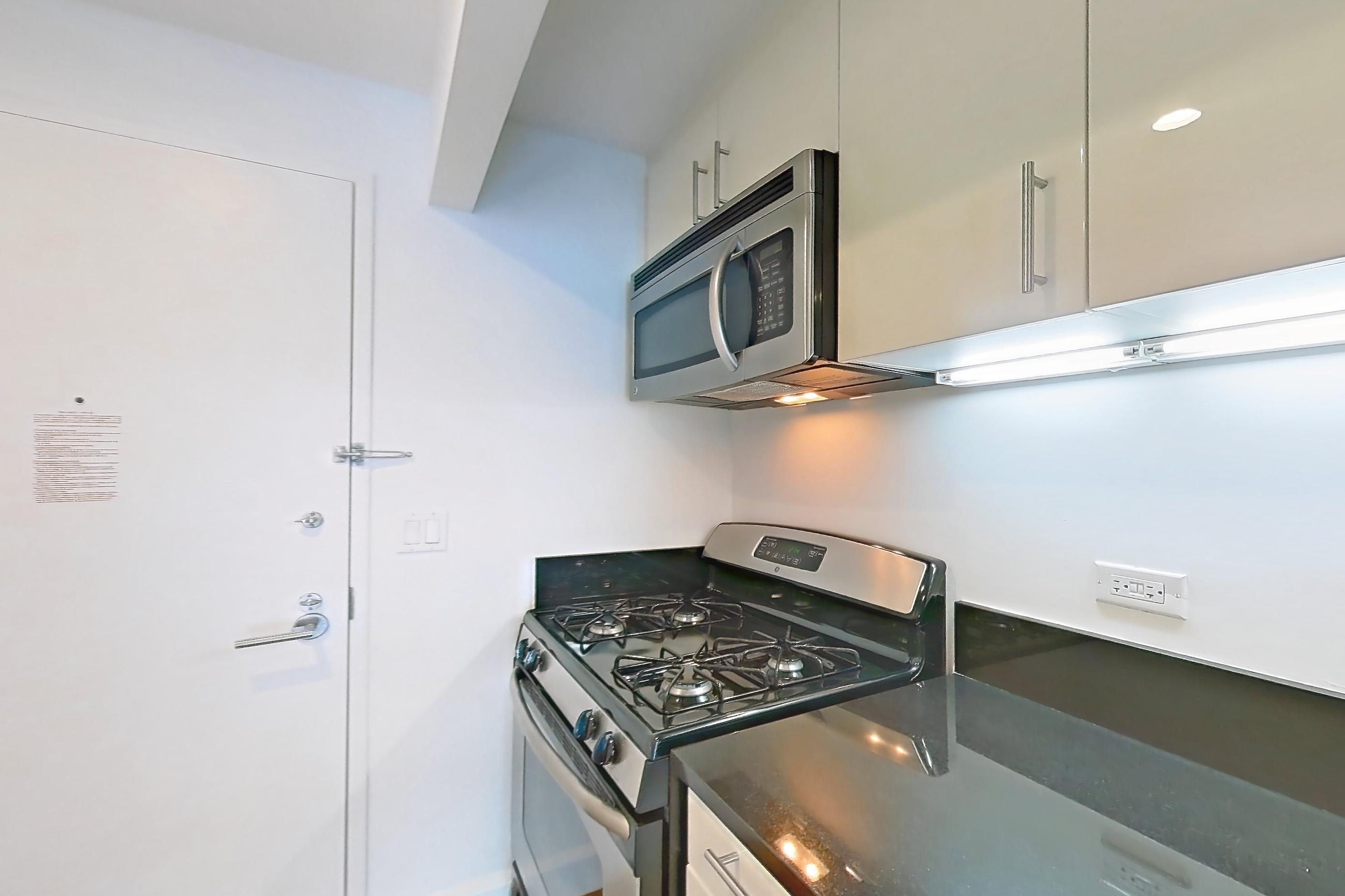 Kitchen with dark countertops, dark stone countertops, dishwasher, gas range, light countertops, light wood-finish flooring, microwave, oven/range, refrigerator, stainless steel appliances, and wood-finish flooring, Apartment 4H at The Addison