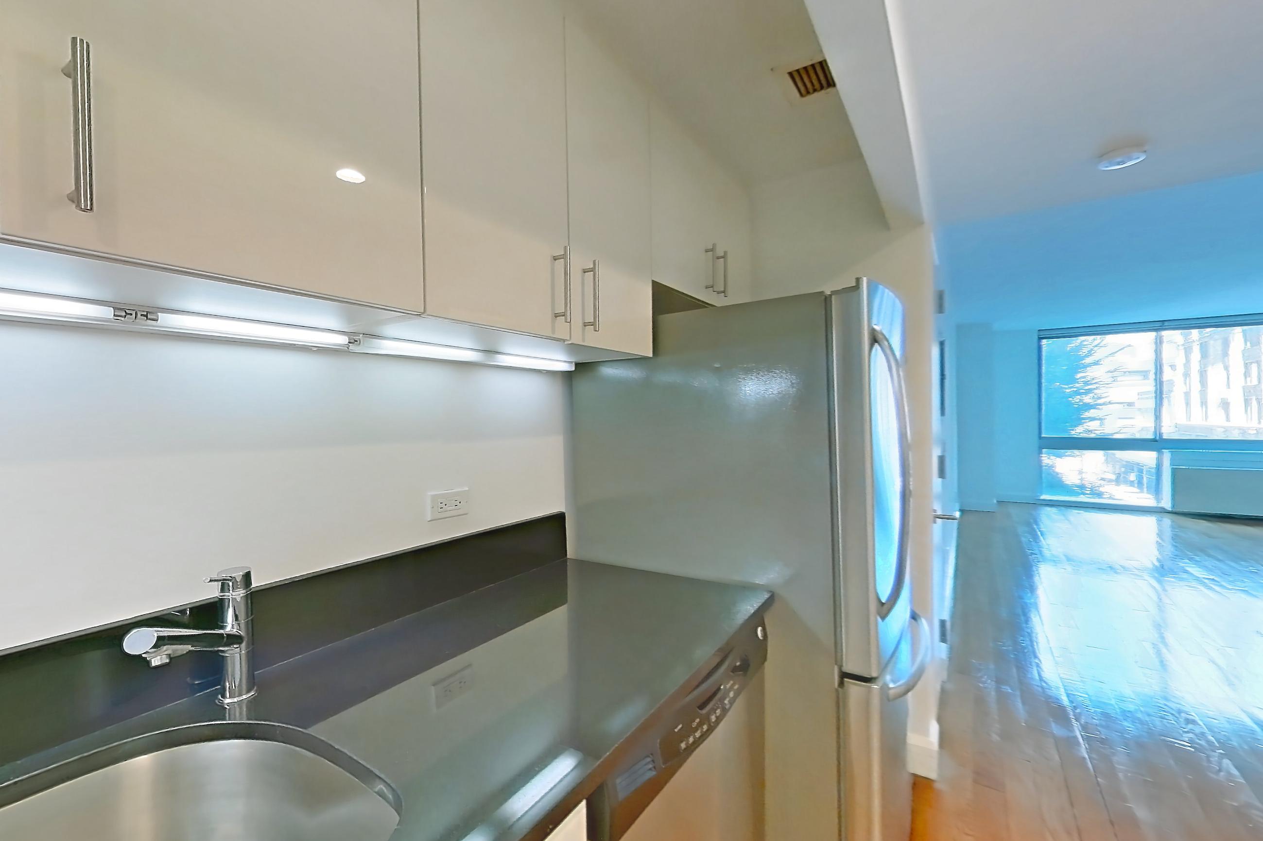 Kitchen with dark countertops, dark stone countertops, dishwasher, gas range, light countertops, light wood-finish flooring, microwave, oven/range, refrigerator, stainless steel appliances, and wood-finish flooring, Apartment 4H at The Addison