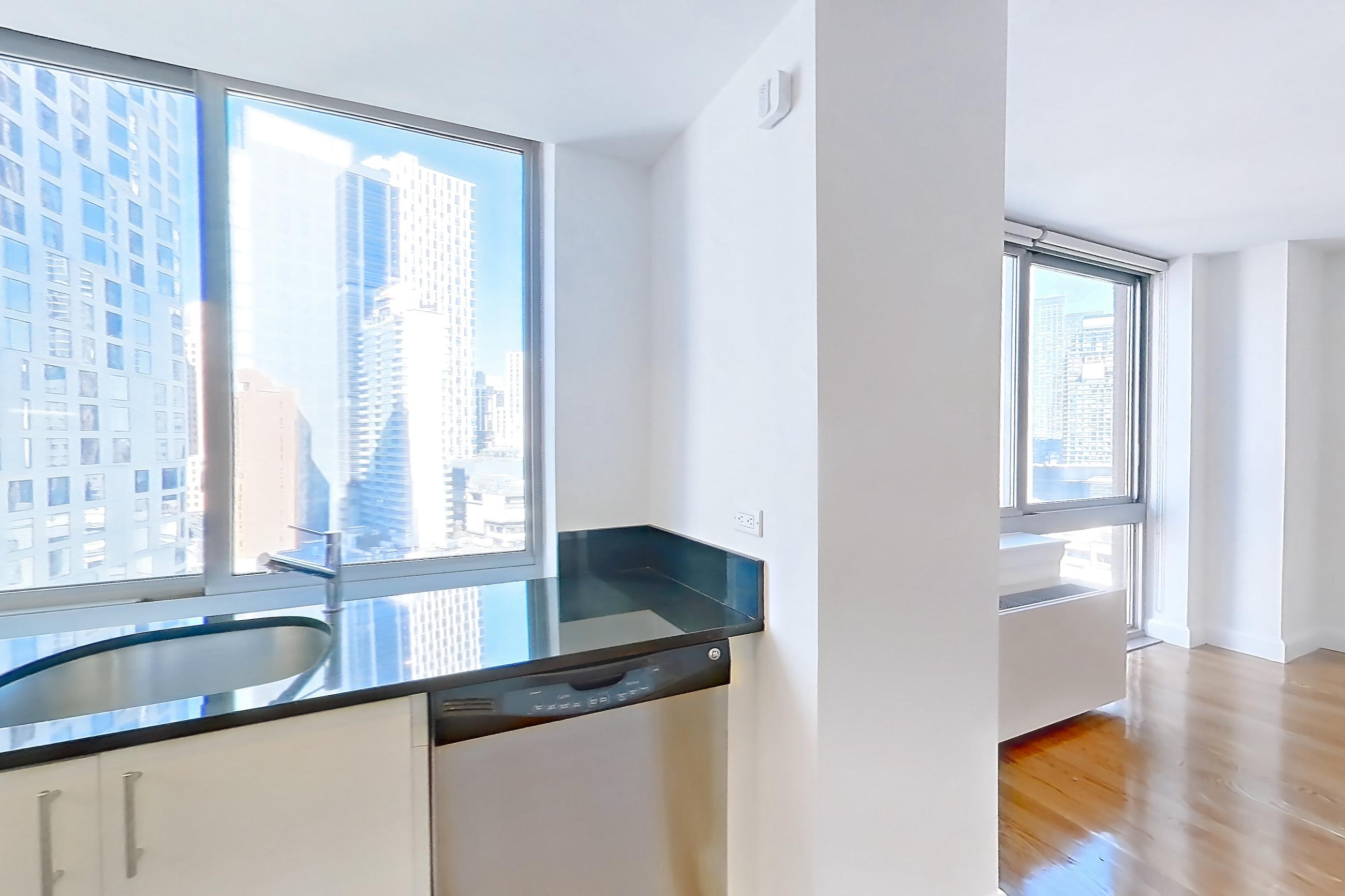 Kitchen with dark countertops, dark stone countertops, dishwasher, gas range, light countertops, light wood-finish flooring, microwave, oven/range, refrigerator, stainless steel appliances, and white appliances, Apartment 18A at The Addison