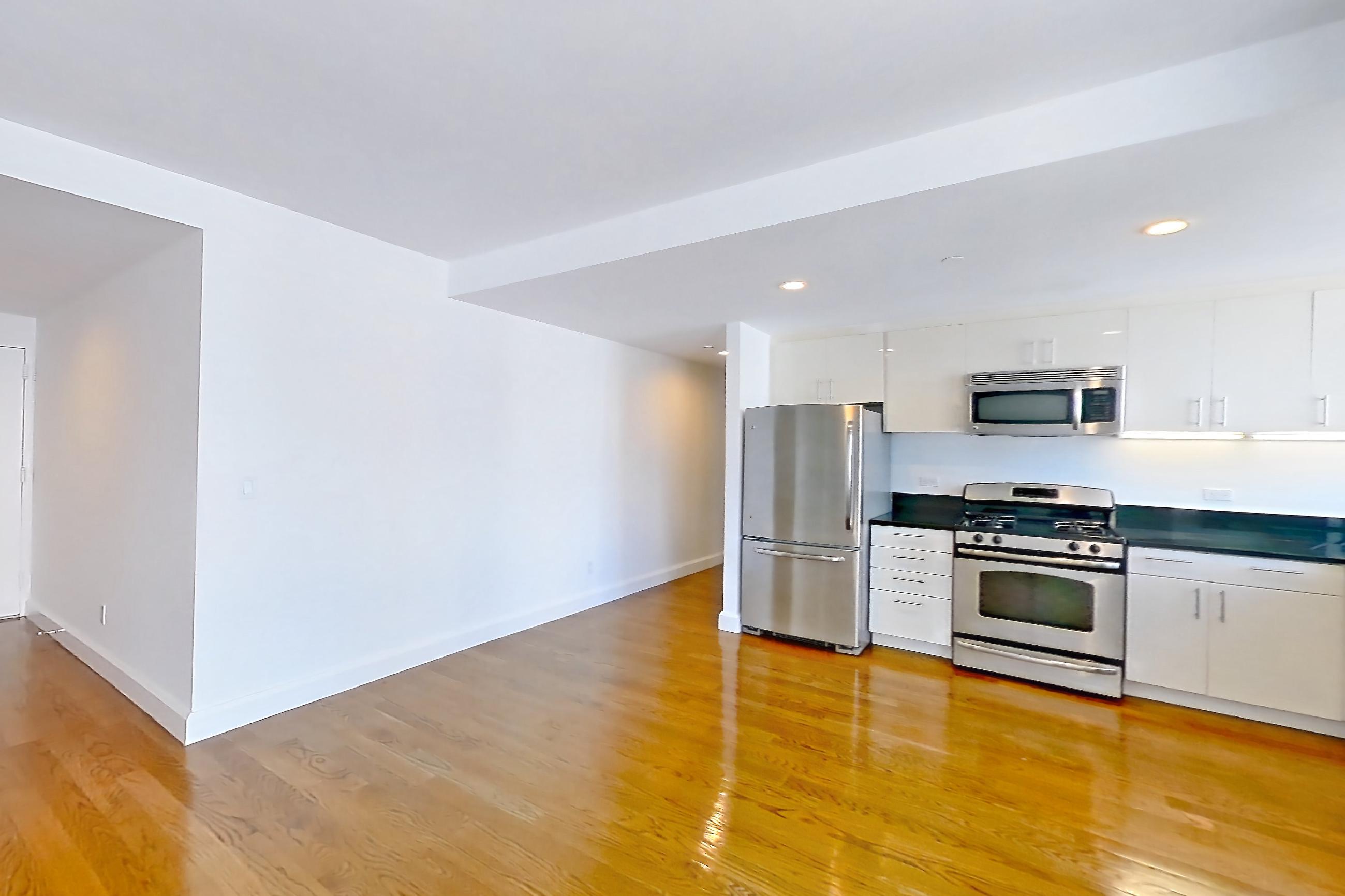Living room with dark countertops, gas range, light countertops, light wood-finish flooring, microwave, oven/range, refrigerator, skyline view, and stainless steel appliances, Apartment 18A at The Addison