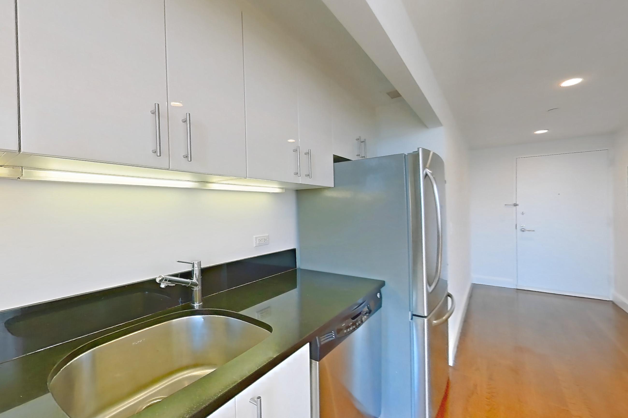 Kitchen with dark countertops, dishwasher, gas range, light countertops, light wood-finish flooring, microwave, oven/range, refrigerator, and stainless steel appliances, Apartment 7K at The Addison