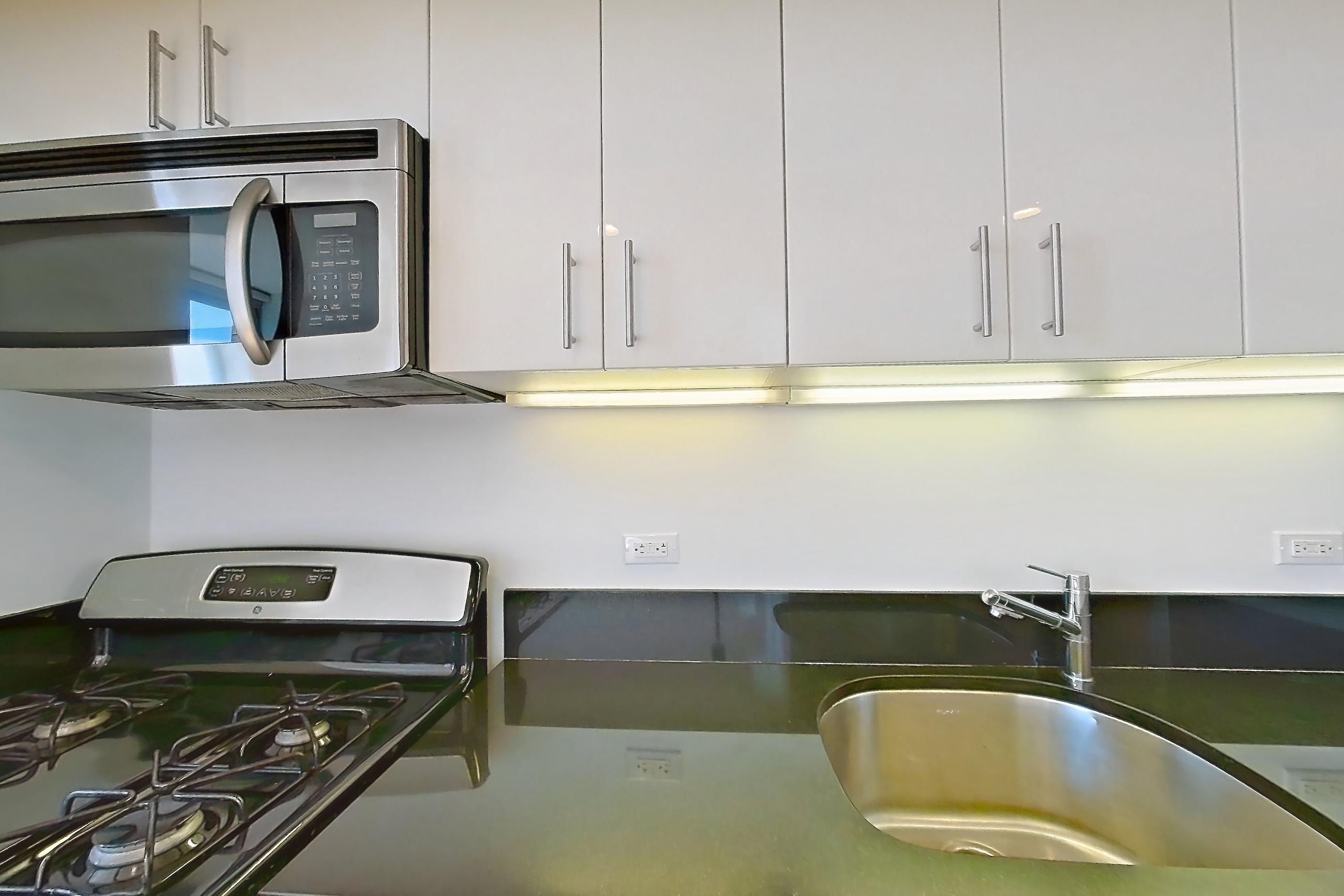 Kitchen with dark countertops, dishwasher, gas range, light countertops, light wood-finish flooring, microwave, oven/range, refrigerator, and stainless steel appliances, Apartment 7K at The Addison