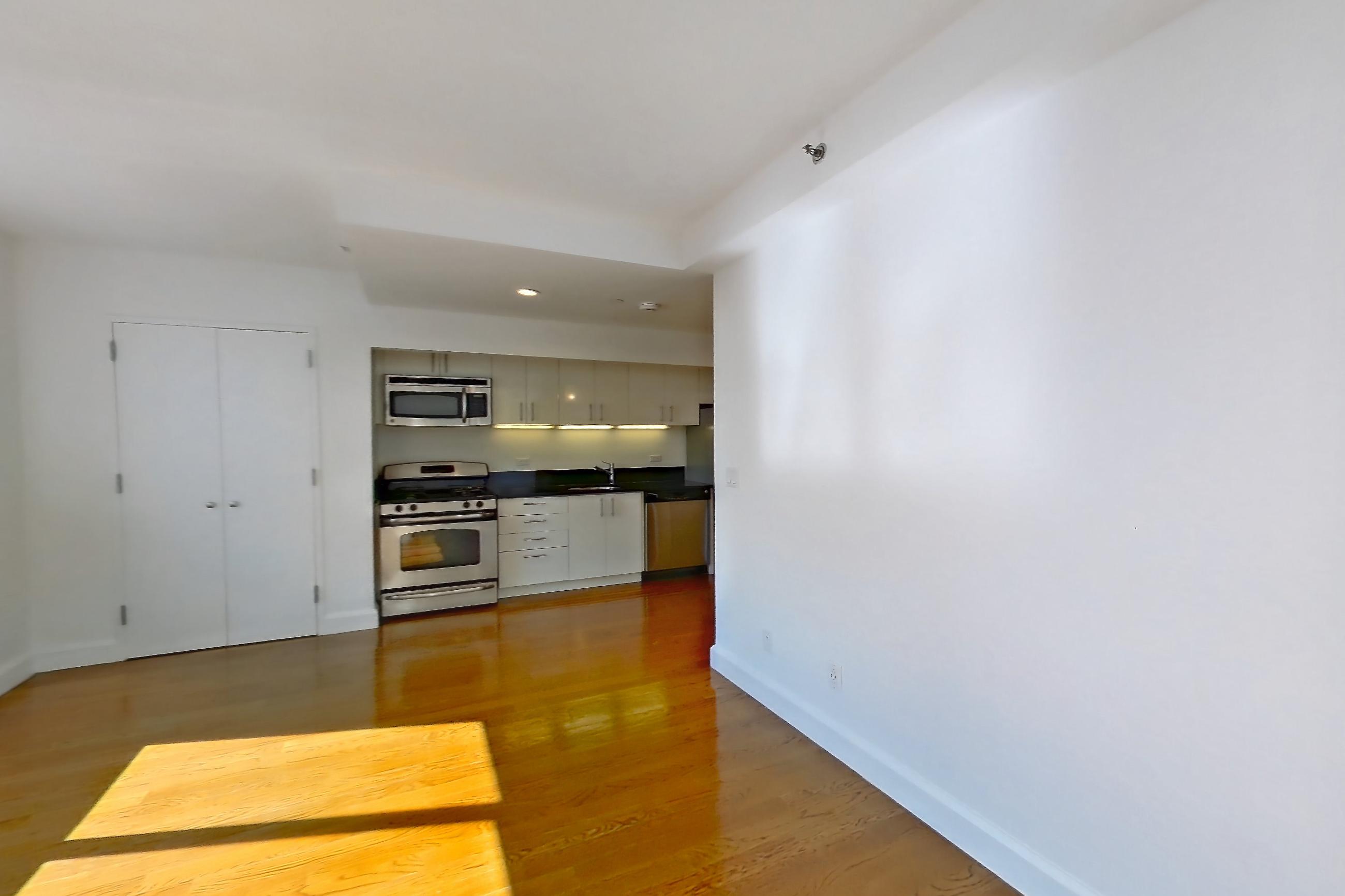 Living room with dark countertops, dishwasher, gas range, light wood-finish flooring, microwave, oven/range, and stainless steel appliances, Apartment 7K at The Addison