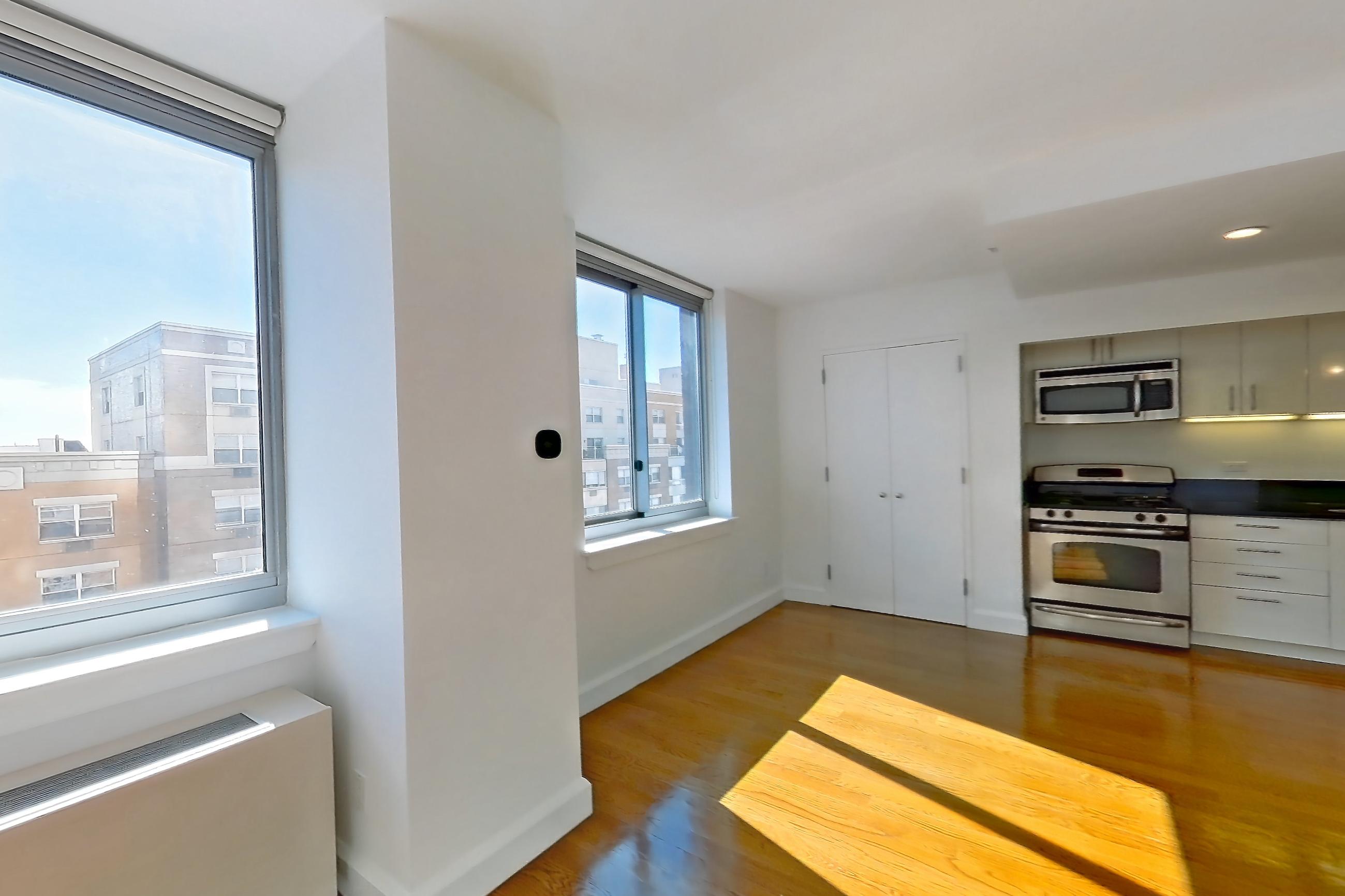 Living room with dark countertops, dishwasher, gas range, light wood-finish flooring, microwave, oven/range, and stainless steel appliances, Apartment 7K at The Addison