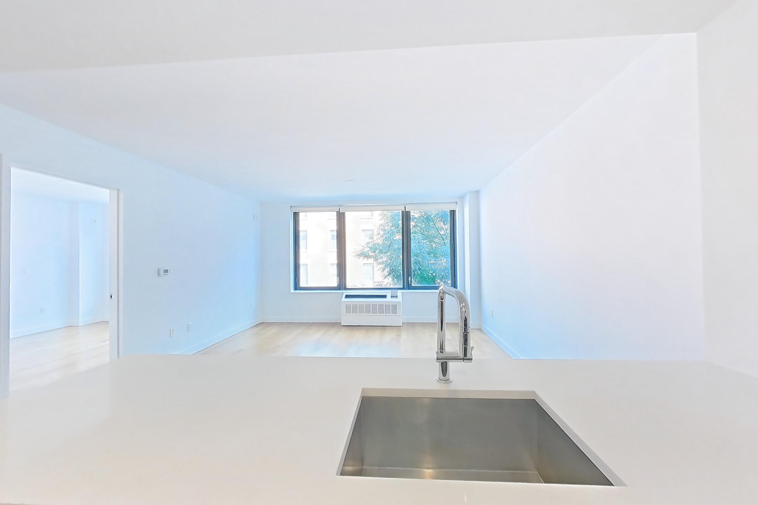Kitchen with black appliances, dishwasher, gas range, kitchen island, light countertops, light stone countertops, light wood-finish flooring, oven/range, refrigerator, and stainless steel appliances, Apartment 307 at The Bergen