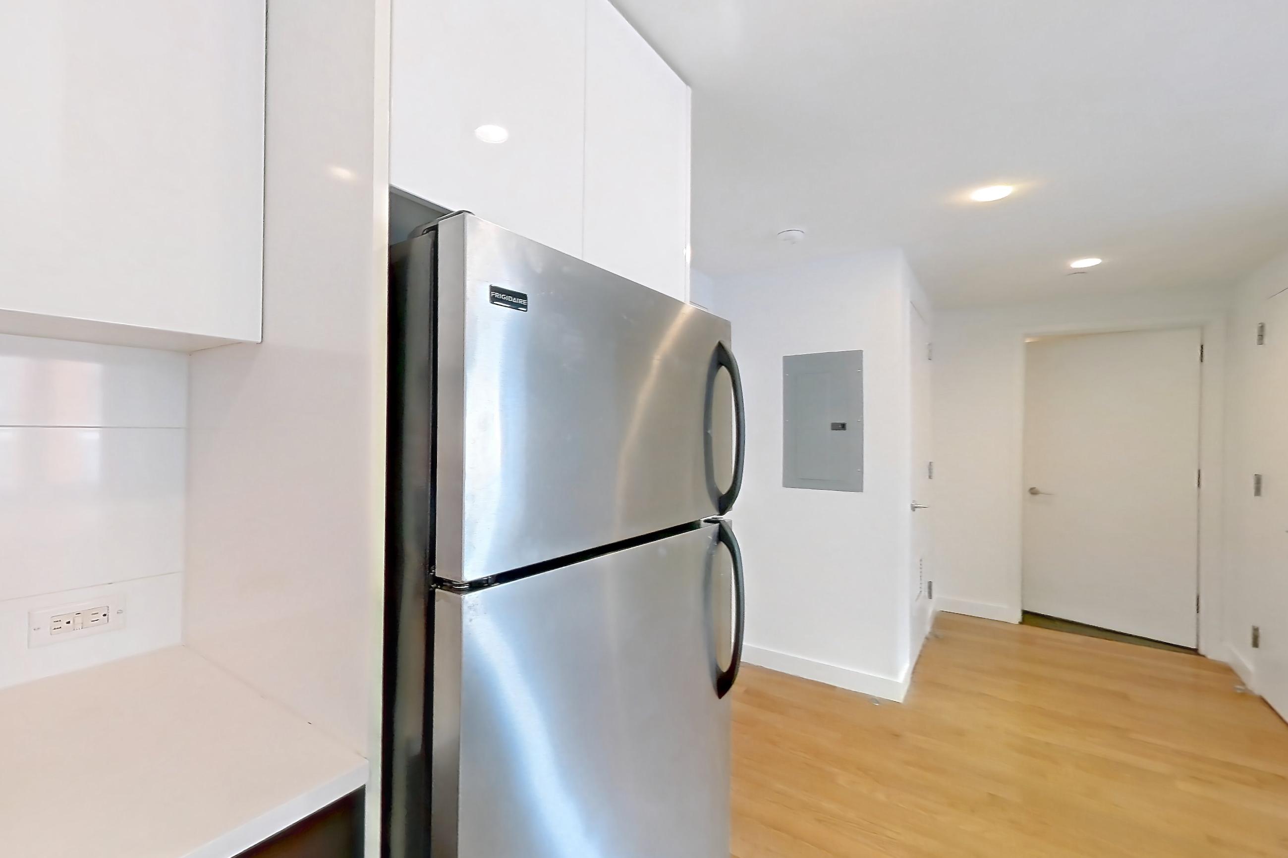 Kitchen with black appliances, dishwasher, gas range, kitchen island, light countertops, light stone countertops, light wood-finish flooring, oven/range, refrigerator, and stainless steel appliances, Apartment 307 at The Bergen