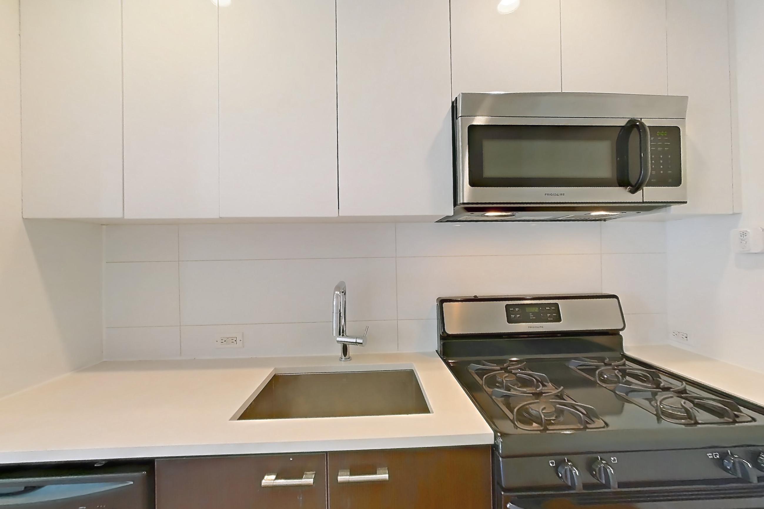 Kitchen with black appliances, dishwasher, gas range, light countertops, light wood-finish flooring, microwave, oven/range, refrigerator, stainless steel appliances, and wood-finish flooring, Apartment 707 at The Bergen
