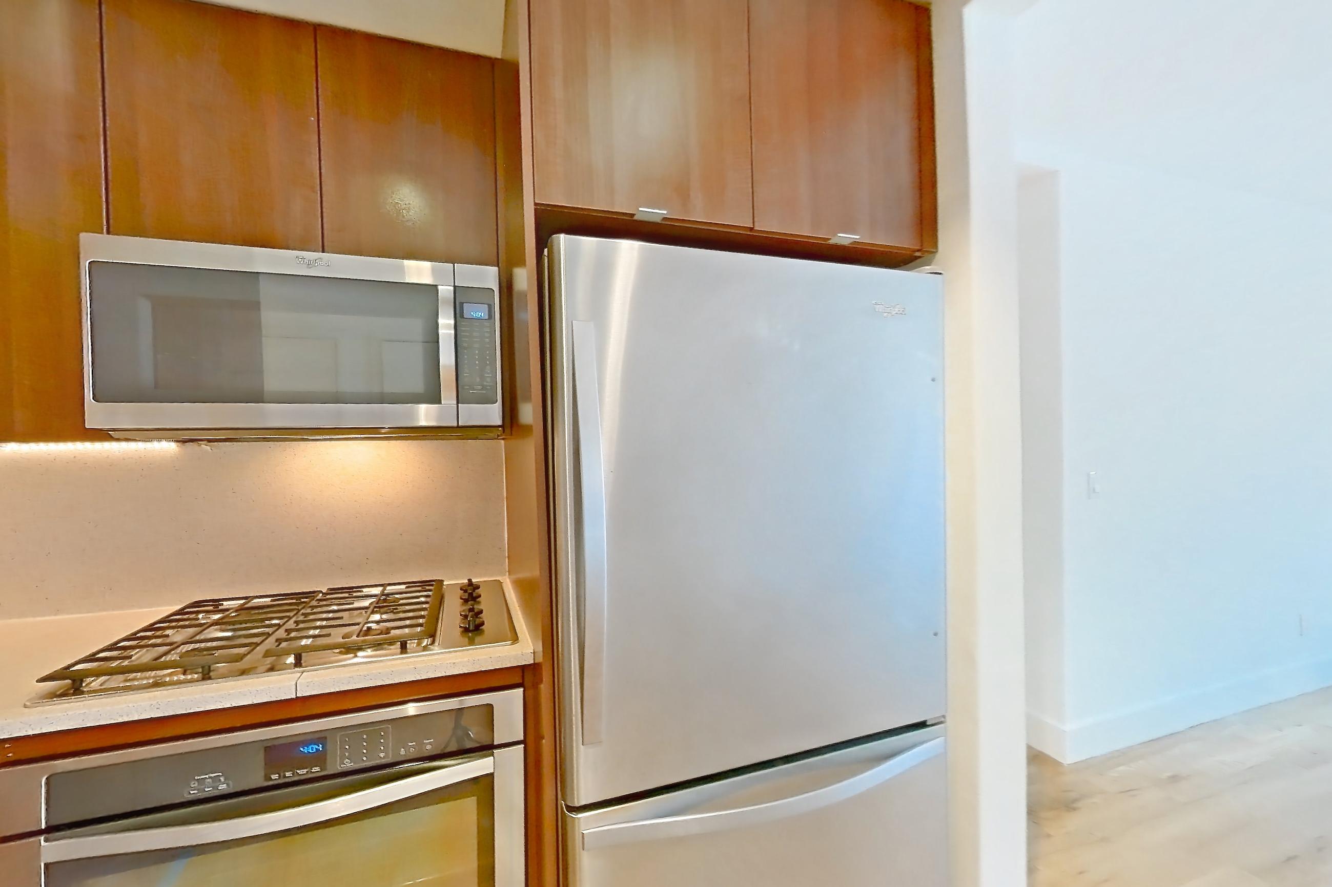 Kitchen with cooktop, dishwasher, gas cooktop, light countertops, light stone countertops, light wood-finish flooring, oven/range, refrigerator, stainless steel appliances, and white appliances, Apartment 6H at The Kestrel