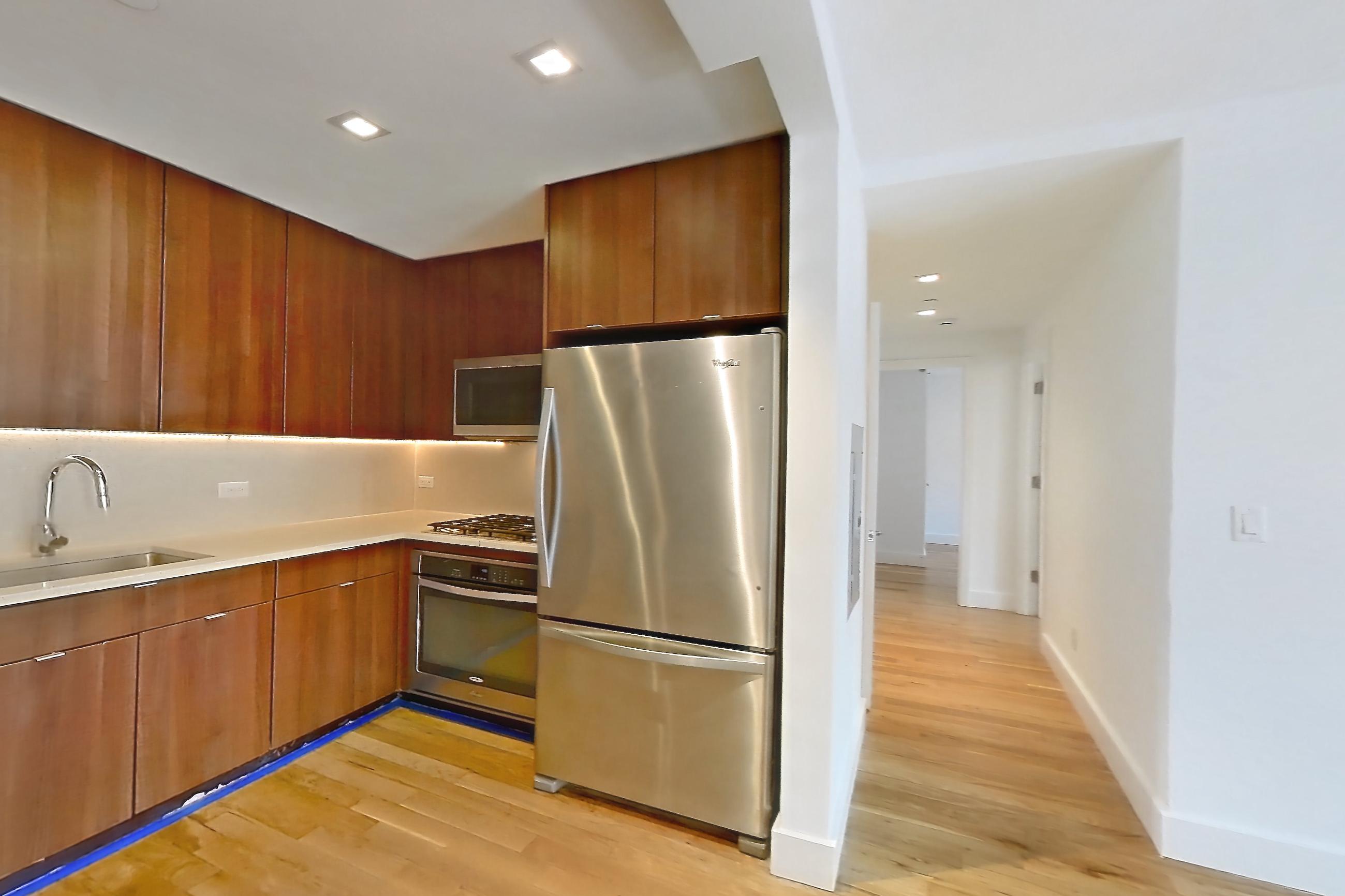 Living space with light countertops, light wood-finish flooring, refrigerator, and stainless steel appliances, Apartment 6H at The Kestrel