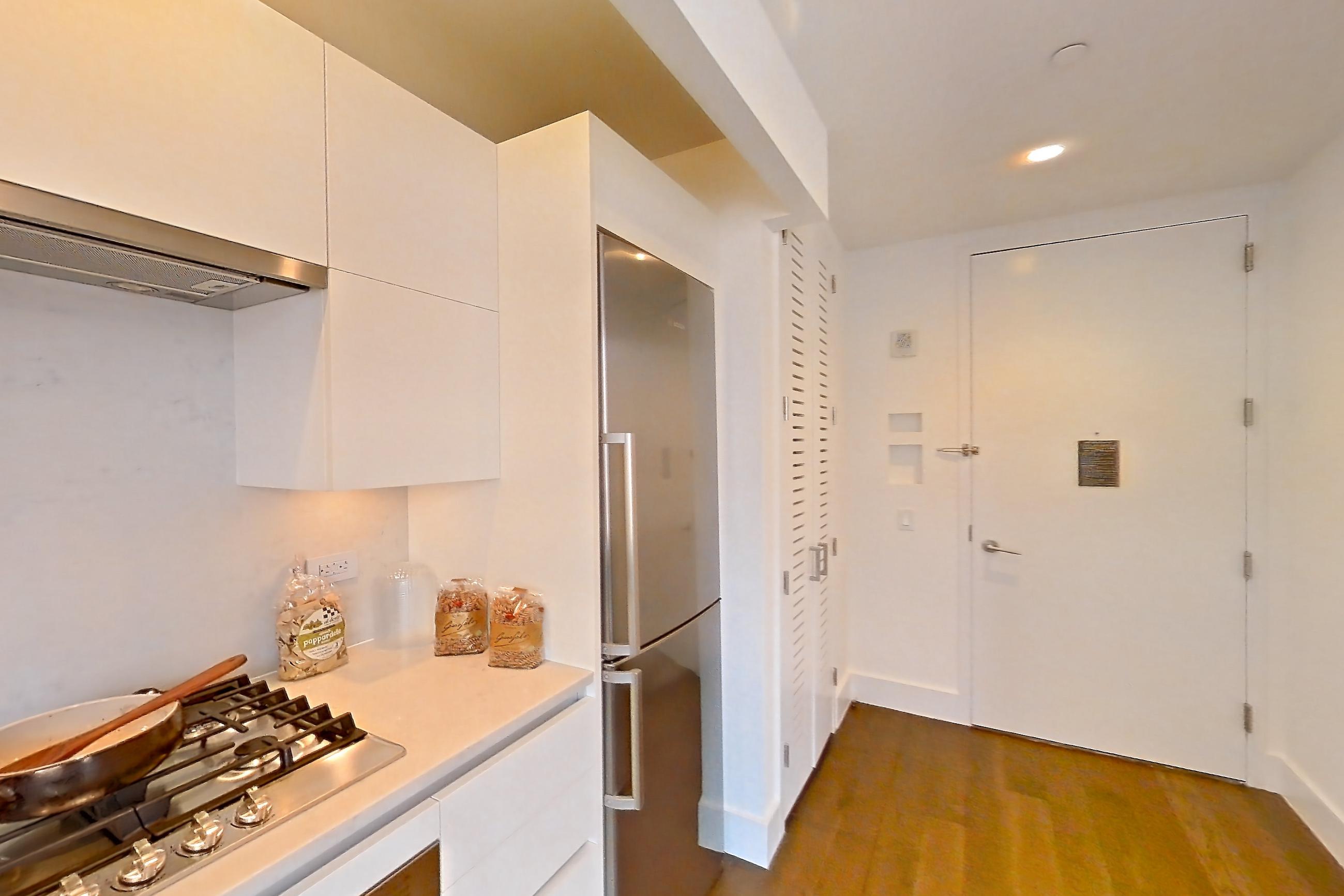 Kitchen with cooktop, dark wood-finish flooring, gas cooktop, light countertops, light stone countertops, oven/range, refrigerator, stainless steel appliances, white appliances, and wood-finish flooring, Apartment 32M at Summit NYC