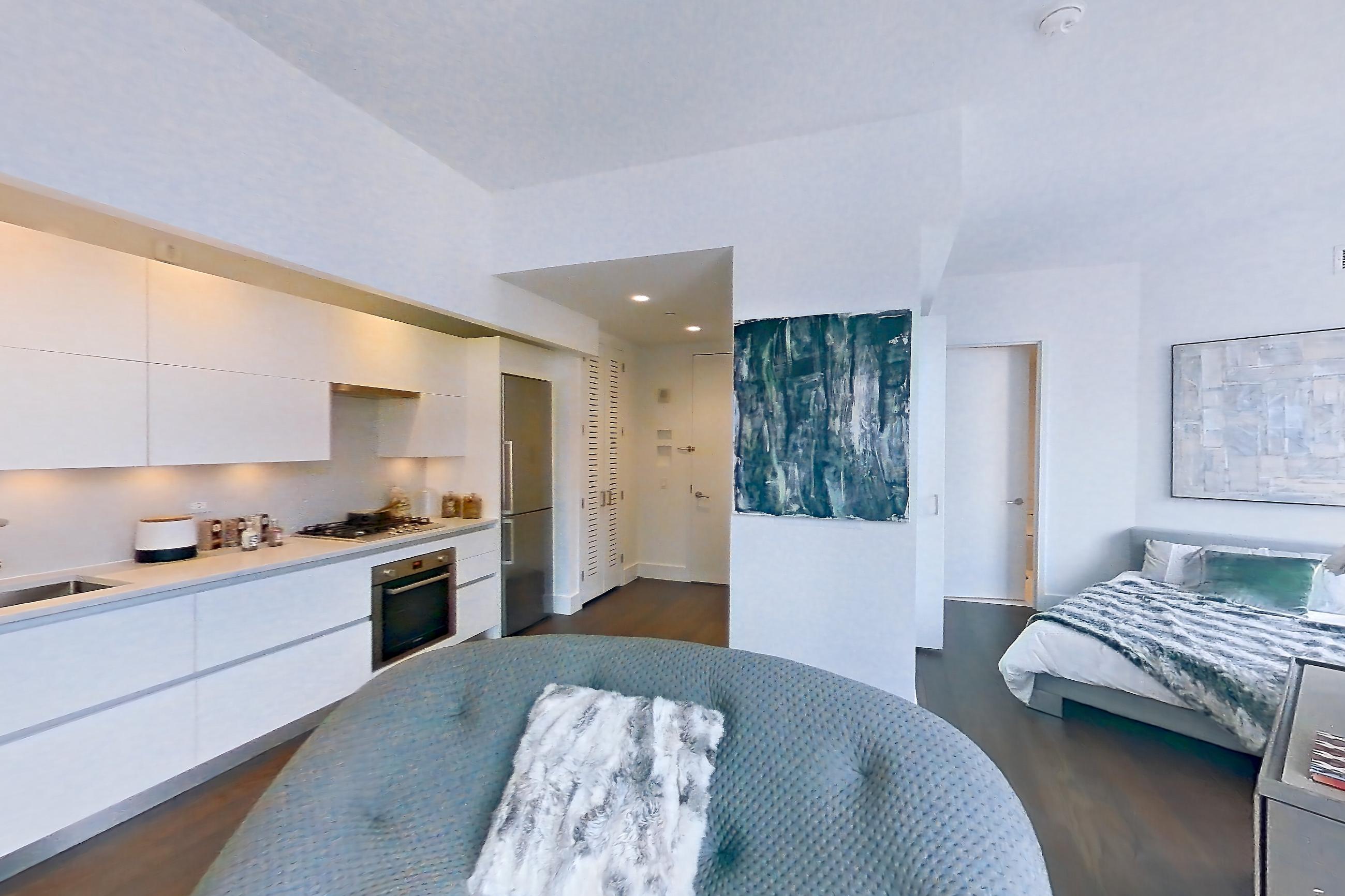 Living room with city view, cooktop, dark wood-finish flooring, gas cooktop, oven/range, refrigerator, skyline view, stainless steel appliances, and wood-finish flooring, Apartment 32M at Summit NYC