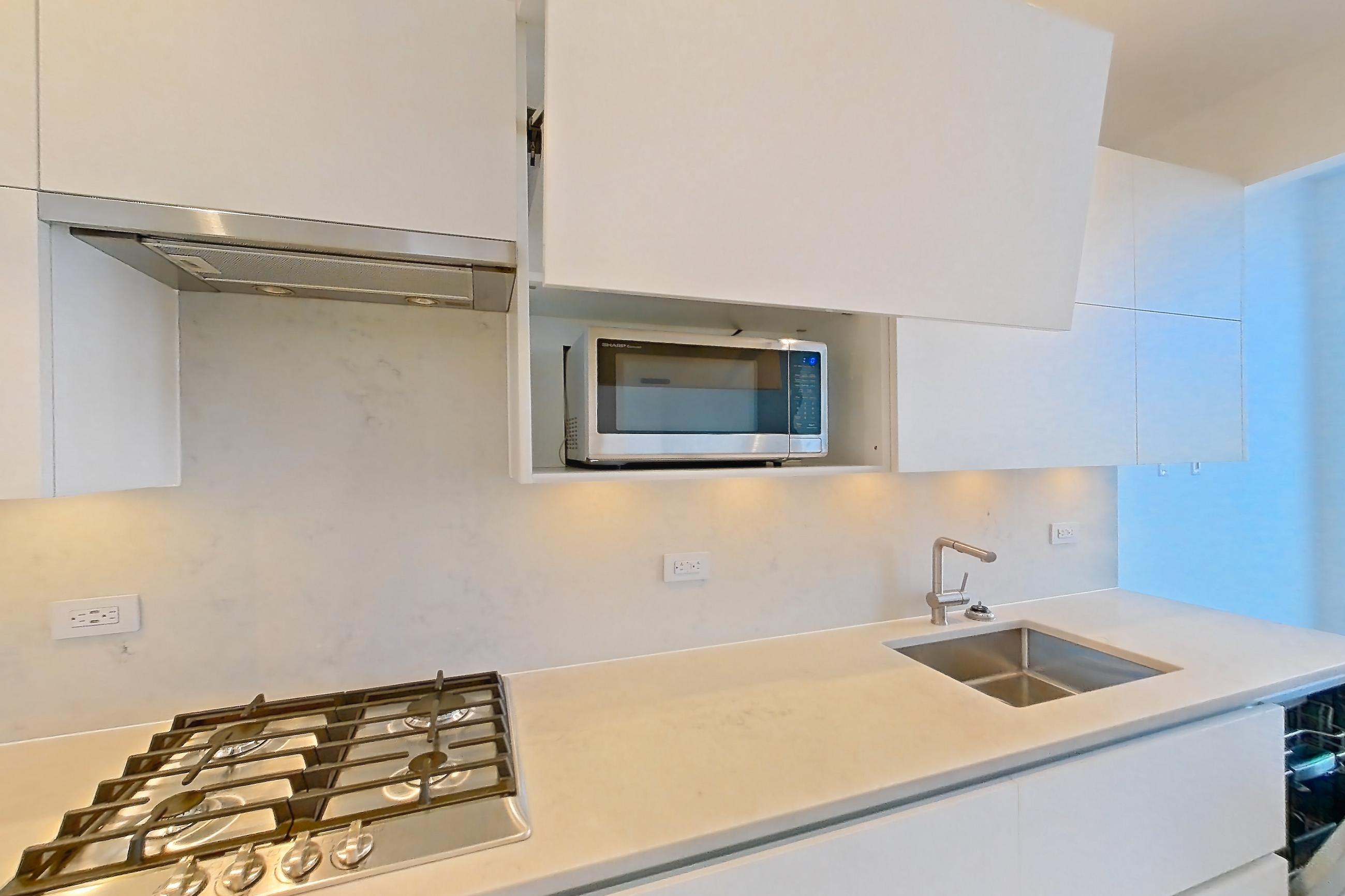Kitchen with cooktop, dark wood-finish flooring, gas cooktop, light countertops, light stone countertops, microwave, oven/range, refrigerator, stainless steel appliances, and wood-finish flooring, Apartment 26H at Summit NYC