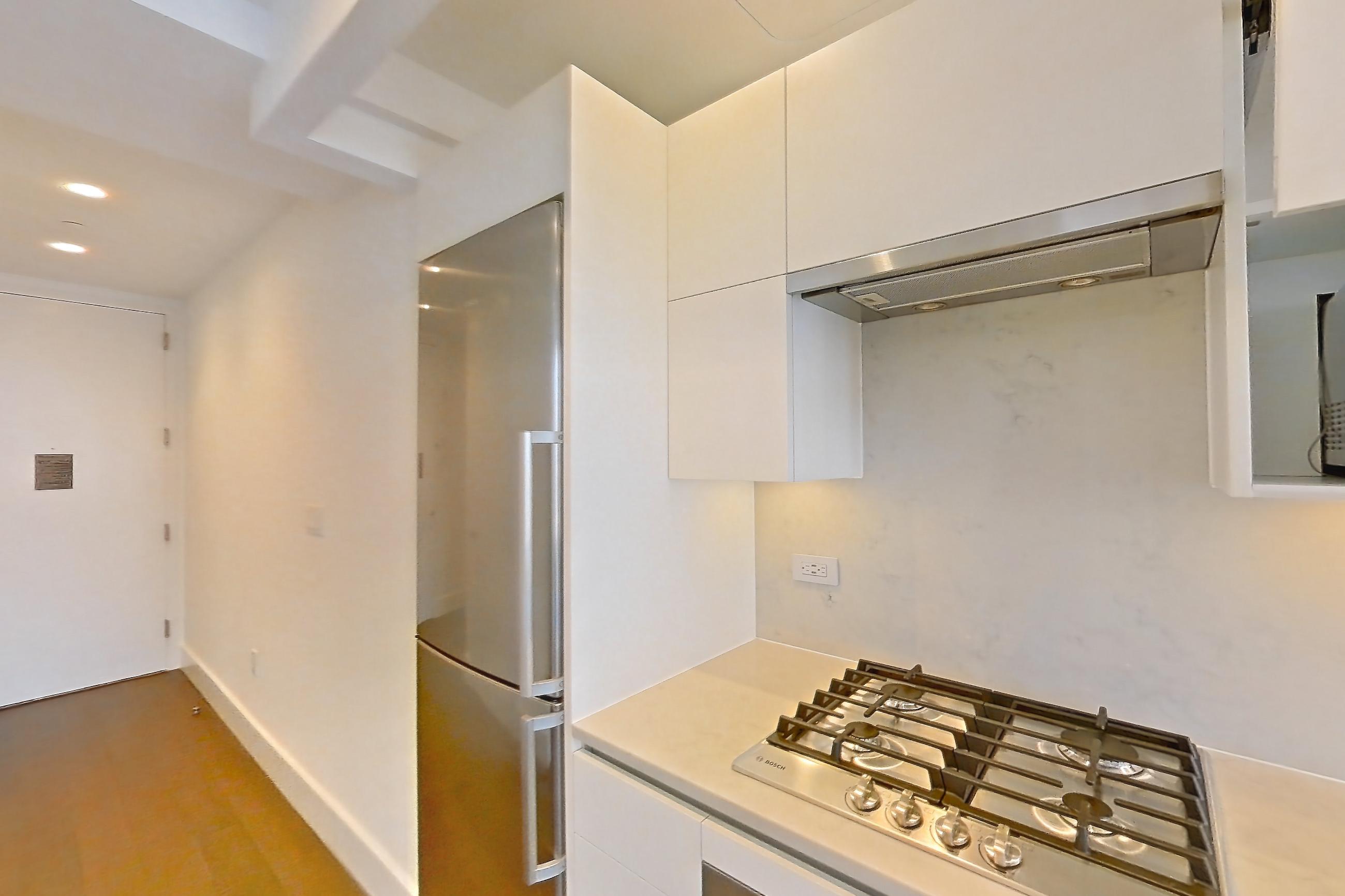 Kitchen with cooktop, dark wood-finish flooring, gas cooktop, light countertops, light stone countertops, microwave, oven/range, refrigerator, stainless steel appliances, and wood-finish flooring, Apartment 26H at Summit NYC