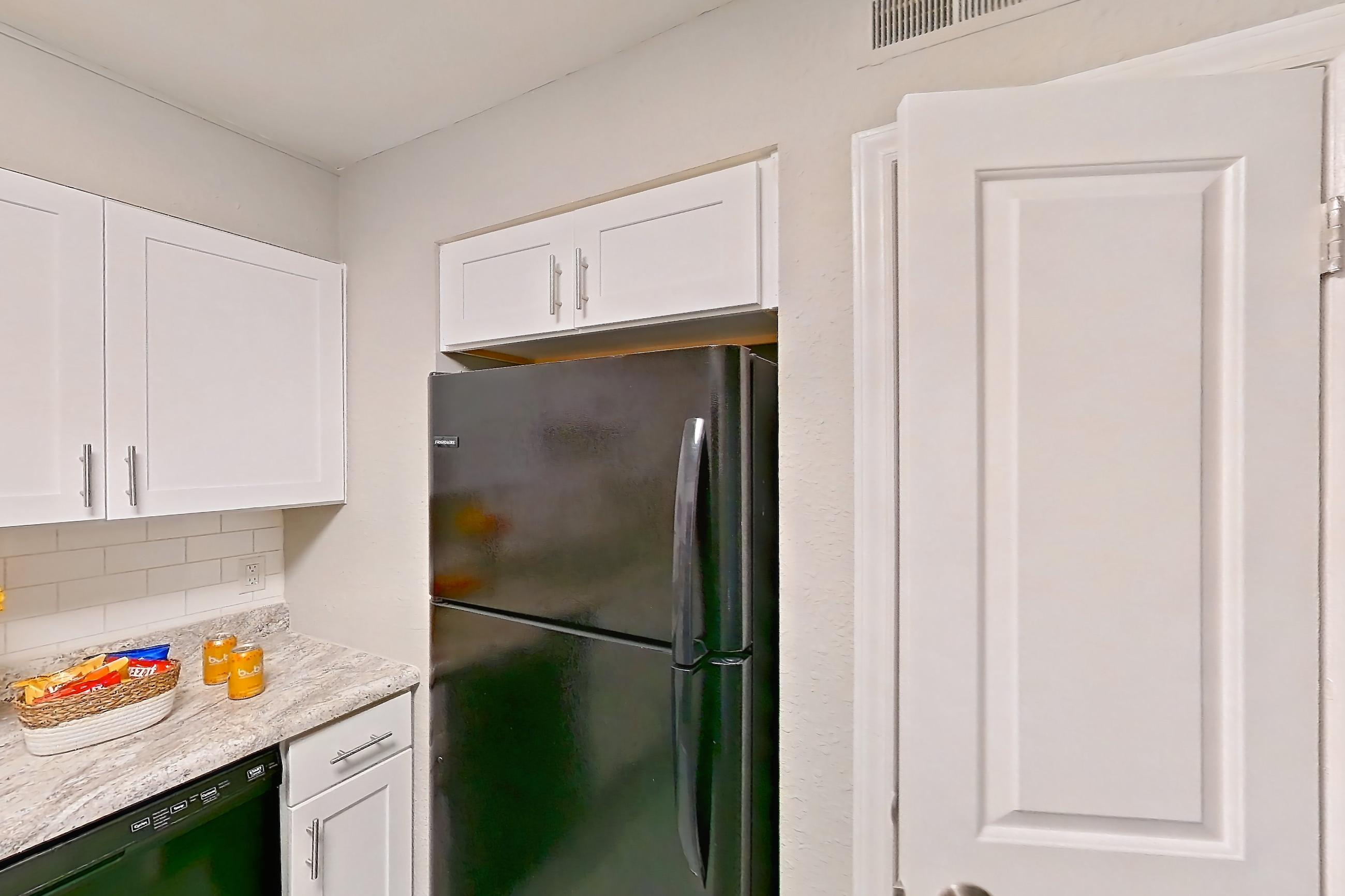 Kitchen with black appliances, dishwasher, gas range, light countertops, light wood-finish flooring, oven/range, range hood, and refrigerator, Unit  1280N at Carriage House & Azalea