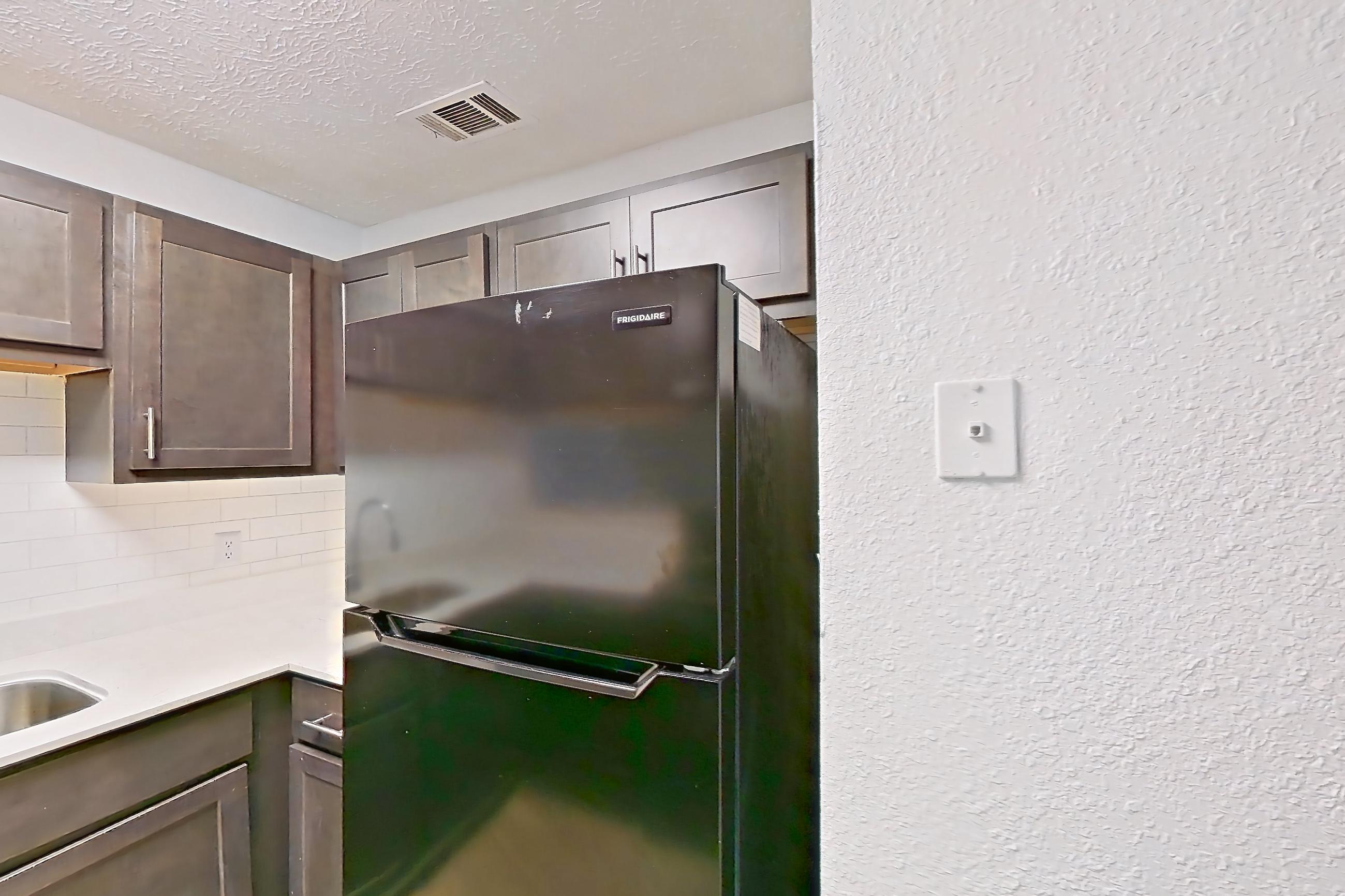 Kitchen with black appliances, electric range, light countertops, light stone countertops, light wood-finish flooring, oven/range, range hood, and refrigerator, Apartment 10 at The Timbers