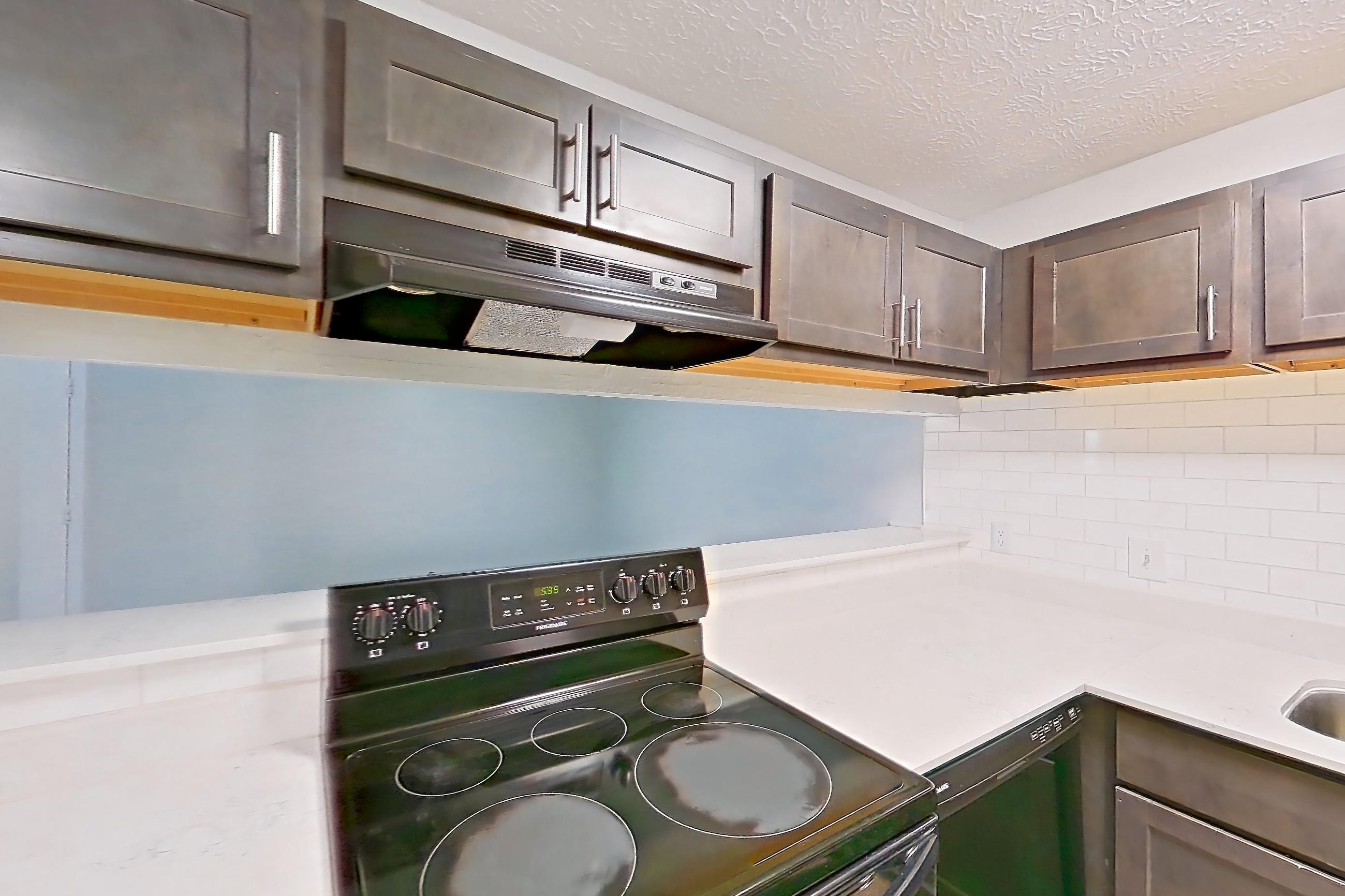 Kitchen with black appliances, electric range, light countertops, light stone countertops, light wood-finish flooring, oven/range, range hood, and refrigerator, Apartment 10 at The Timbers