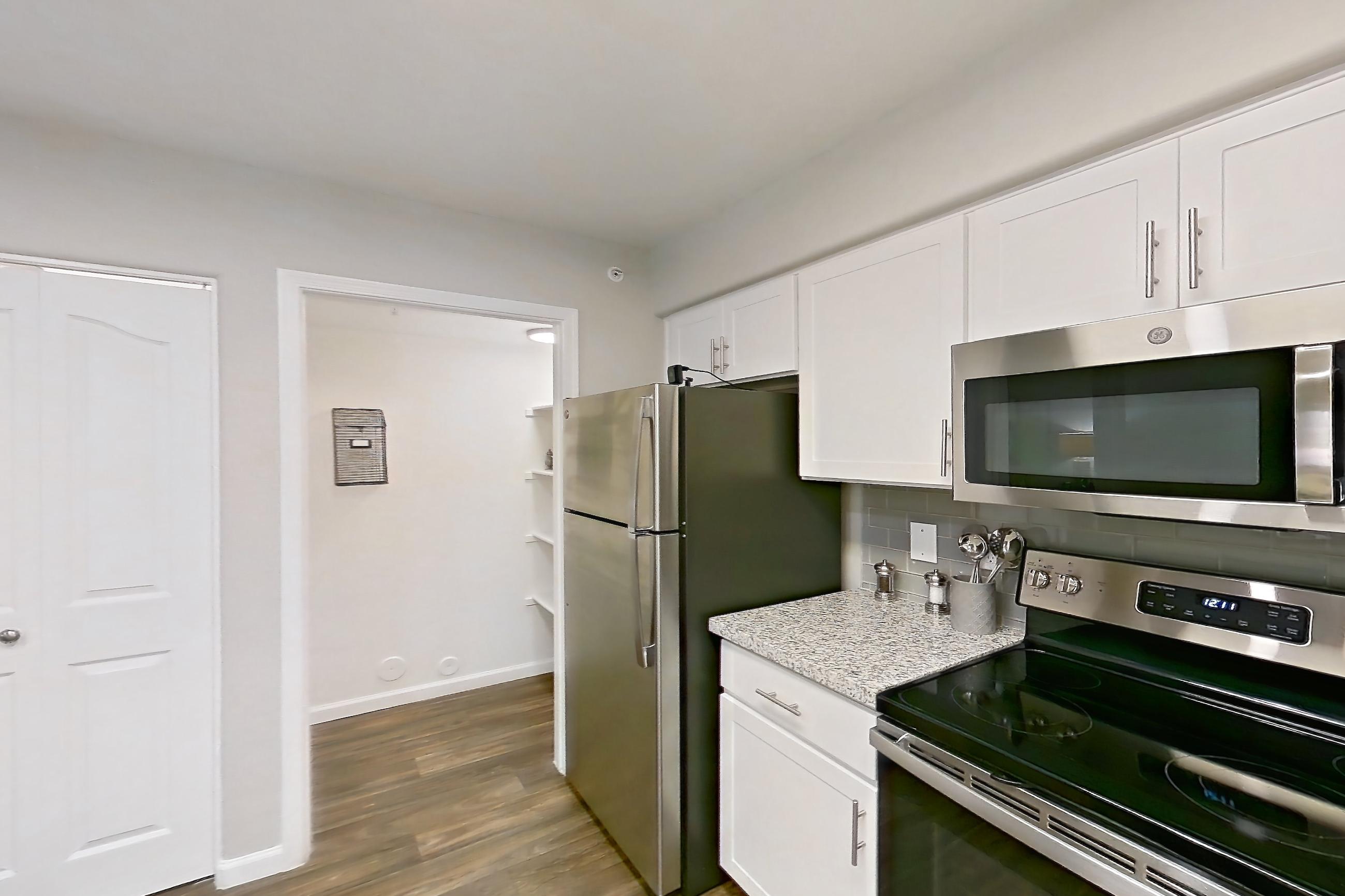 Kitchen with dark wood-finish flooring, dishwasher, electric range, light countertops, light stone countertops, oven/range, refrigerator, and stainless steel appliances, Apartment 1013 at The Palms On Scottsdale