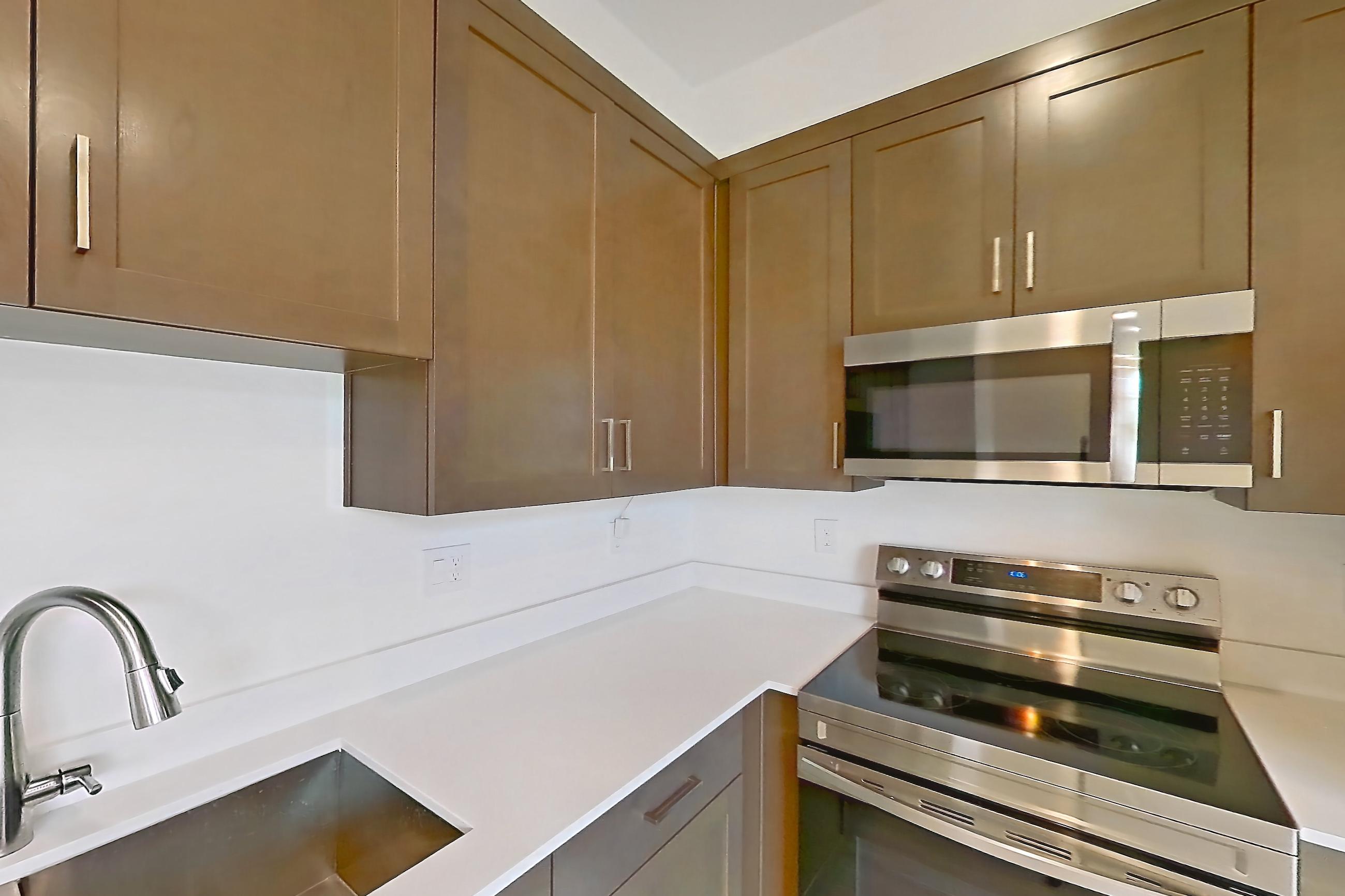 Kitchen with dishwasher, electric range, light countertops, light wood-finish flooring, microwave, oven/range, refrigerator, stainless steel appliances, and water & ice dispenser, Apartment 1A at Tavalo At Cadence