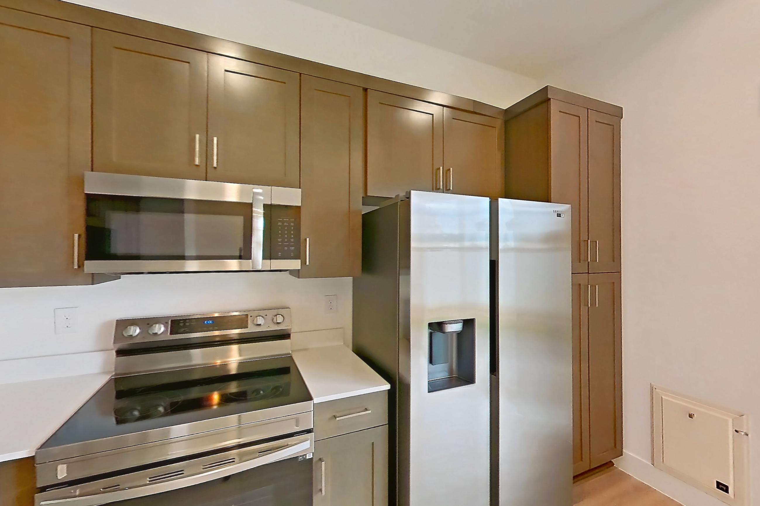 Kitchen with dishwasher, electric range, light countertops, light wood-finish flooring, microwave, oven/range, refrigerator, stainless steel appliances, and water & ice dispenser, Apartment 1A at Tavalo At Cadence