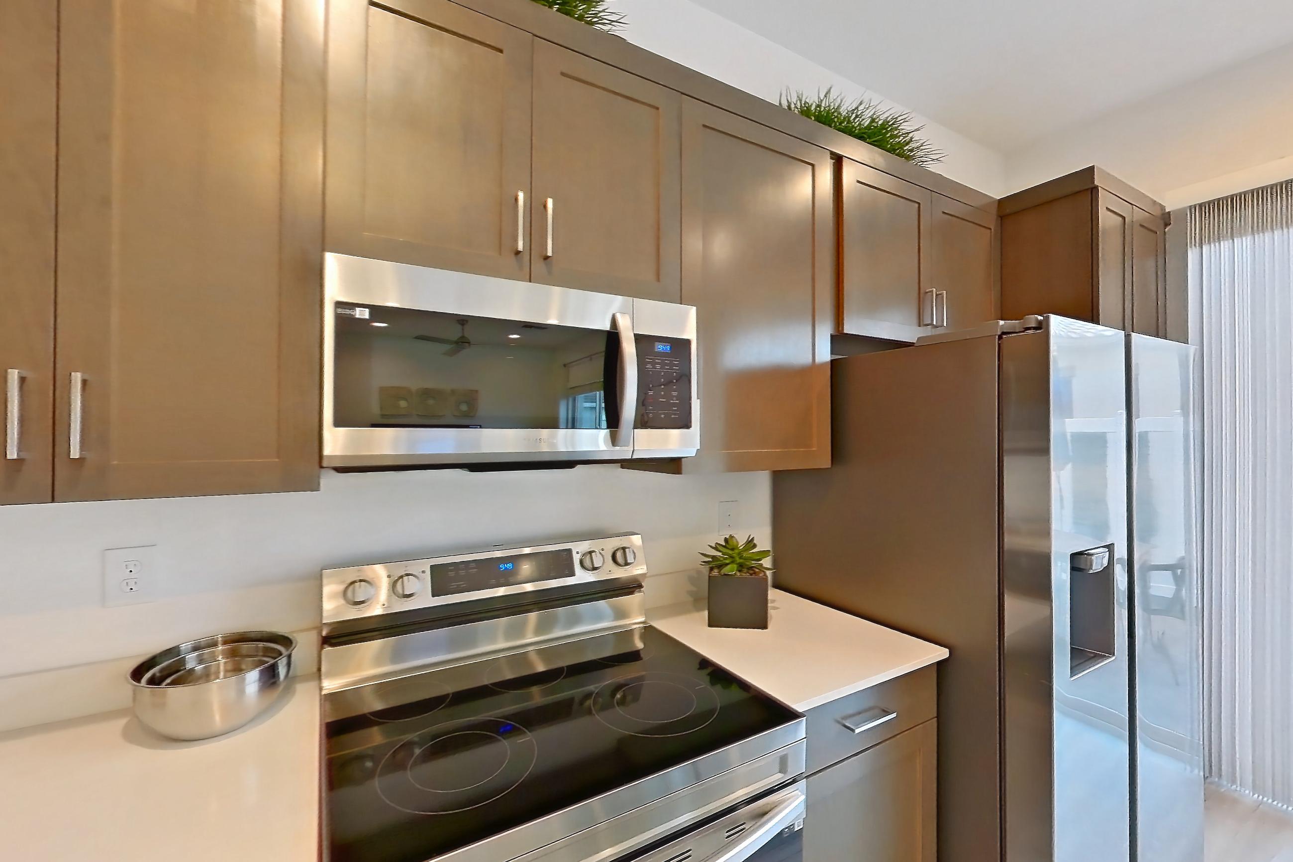 Kitchen with dishwasher, electric range, light countertops, light wood-finish flooring, microwave, oven/range, refrigerator, stainless steel appliances, water & ice dispenser, and white appliances, Apartment 2A at Tavalo At Cadence