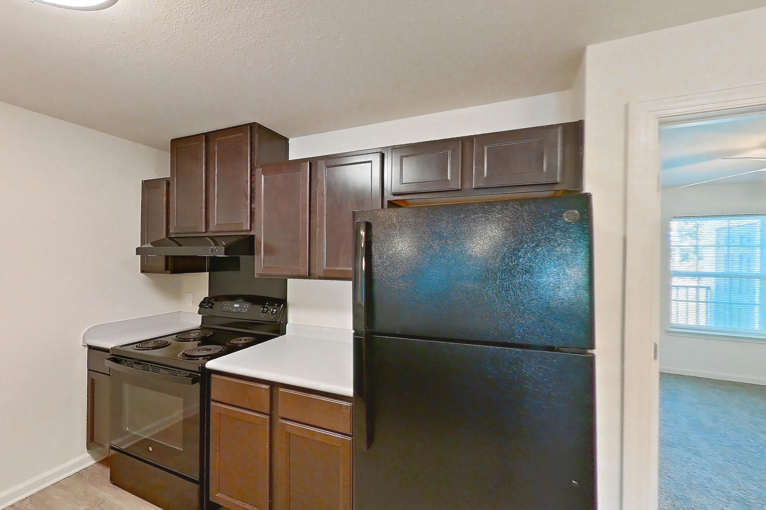 Kitchen with black appliances, electric range, light carpet, light countertops, light wood-finish flooring, oven/range, and refrigerator, Apartment 10O at Springbrook