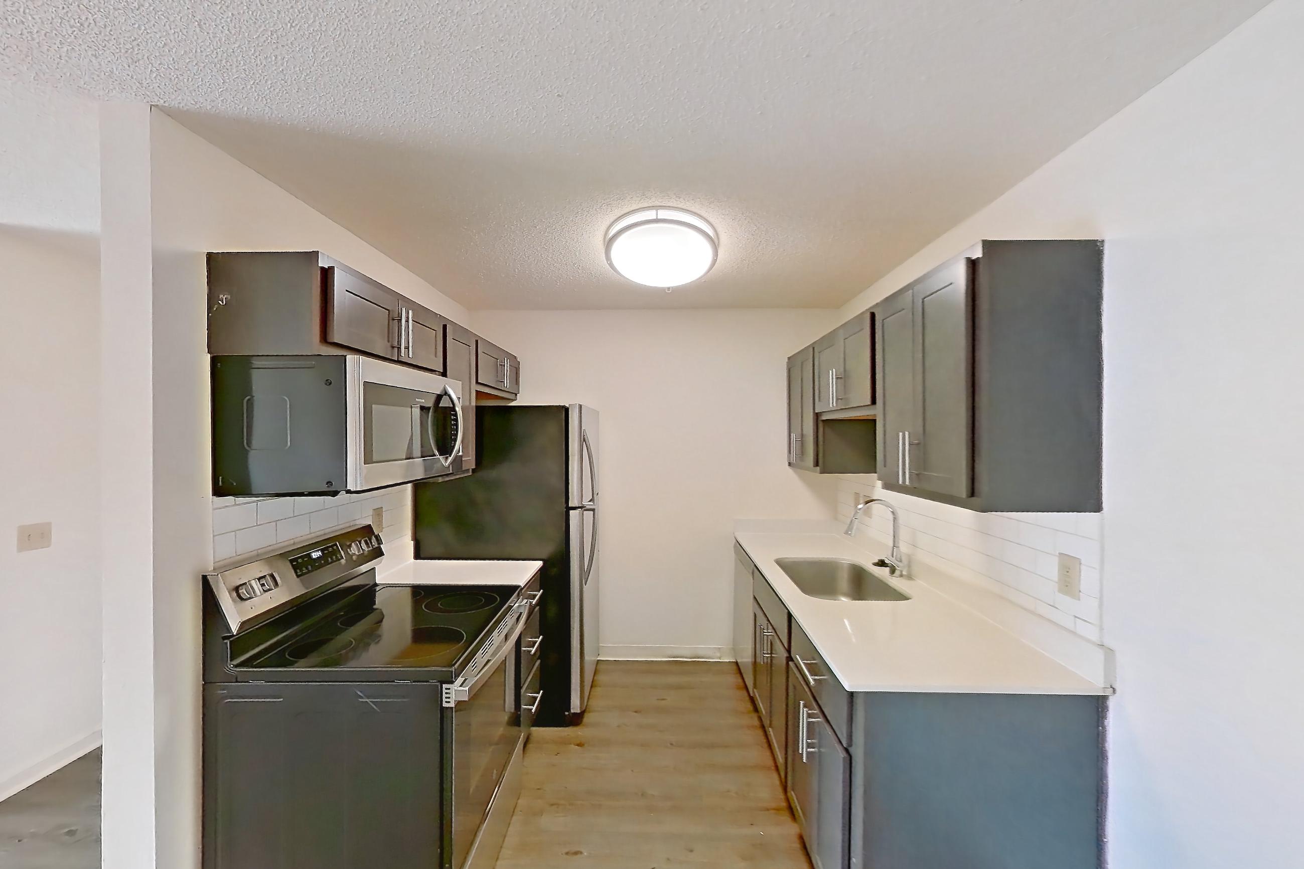 Dining room with dark wood-finish flooring, light countertops, light stone countertops, refrigerator, and stainless steel appliances, Apartment 2225-B at The Landings