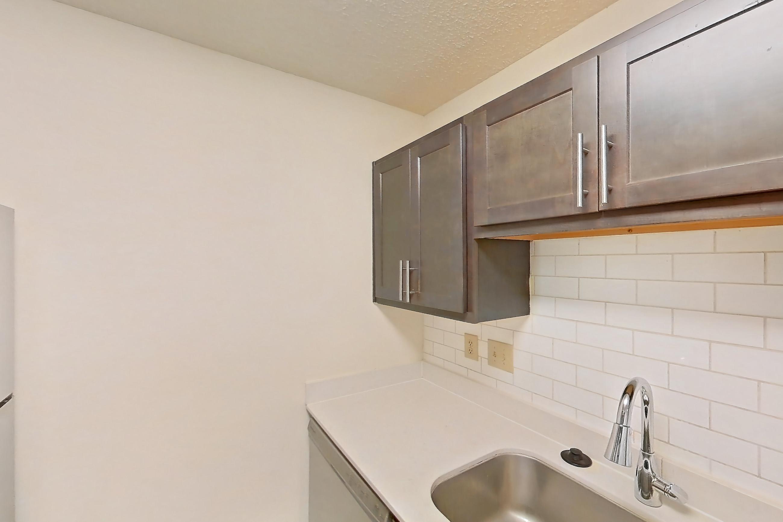 Kitchen with dark wood-finish flooring, electric range, light countertops, light stone countertops, light wood-finish flooring, microwave, oven/range, refrigerator, and stainless steel appliances, Apartment 2225-B at The Landings